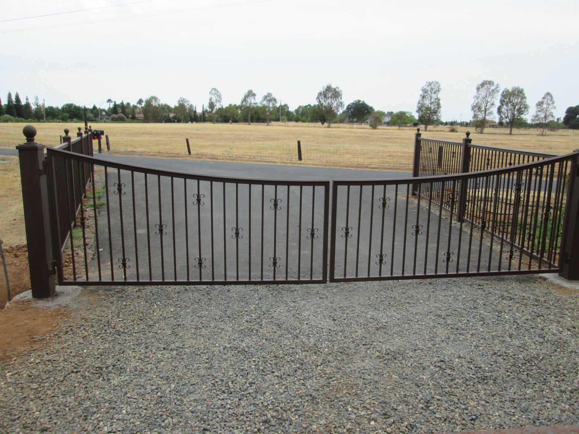 A wrought iron gate is open to a gravel driveway