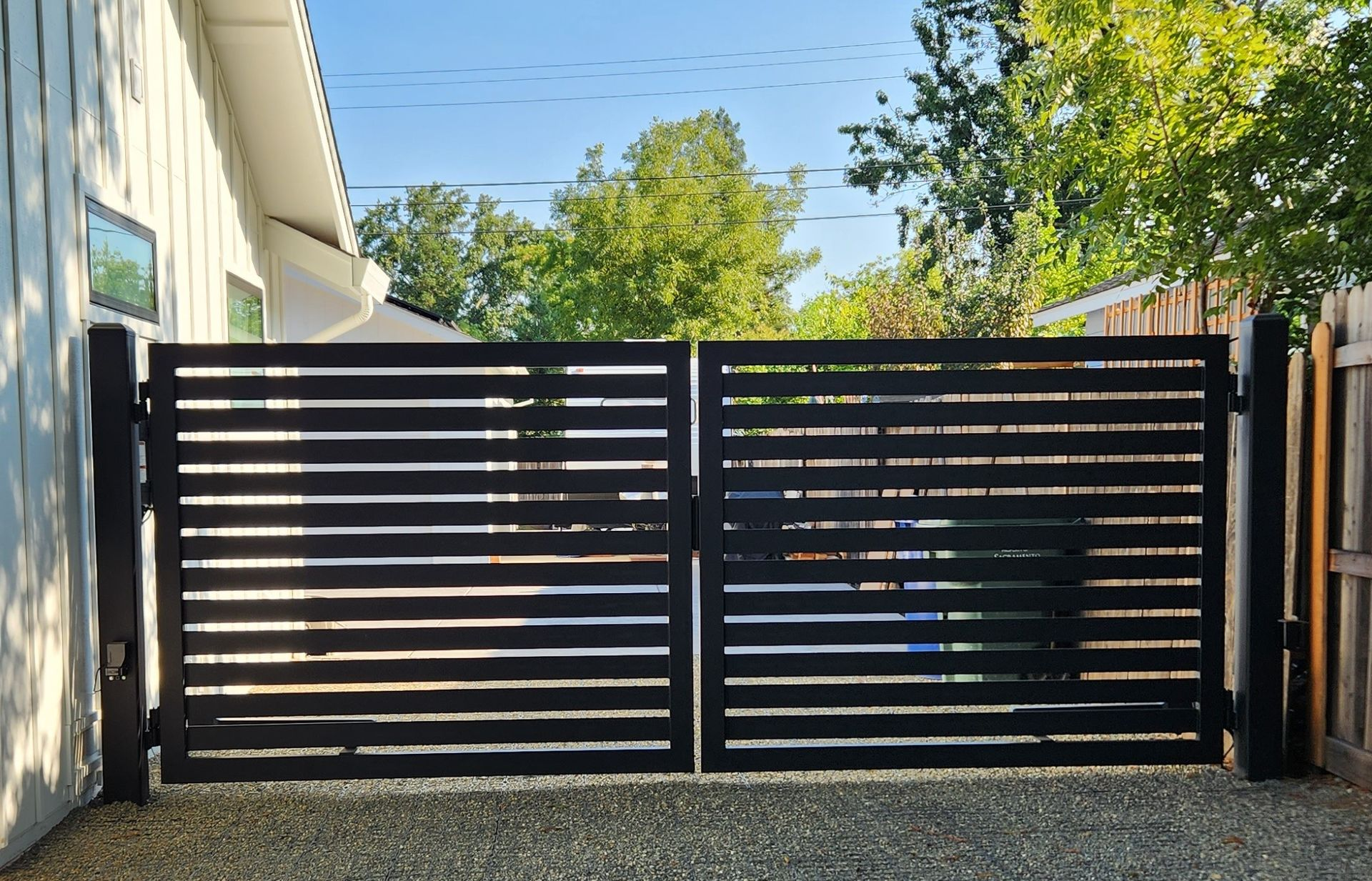 A black gate is open to a driveway in front of a house