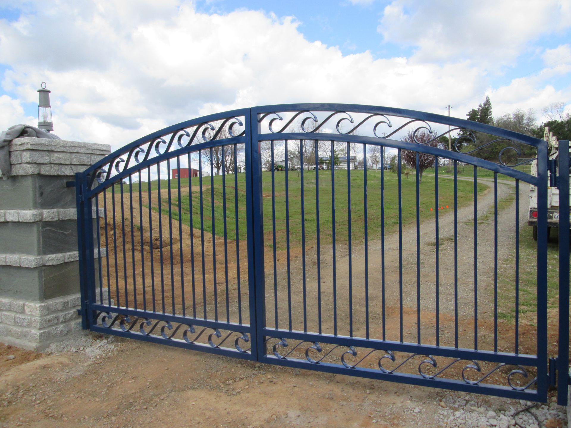 A blue wrought iron gate is open to a dirt road