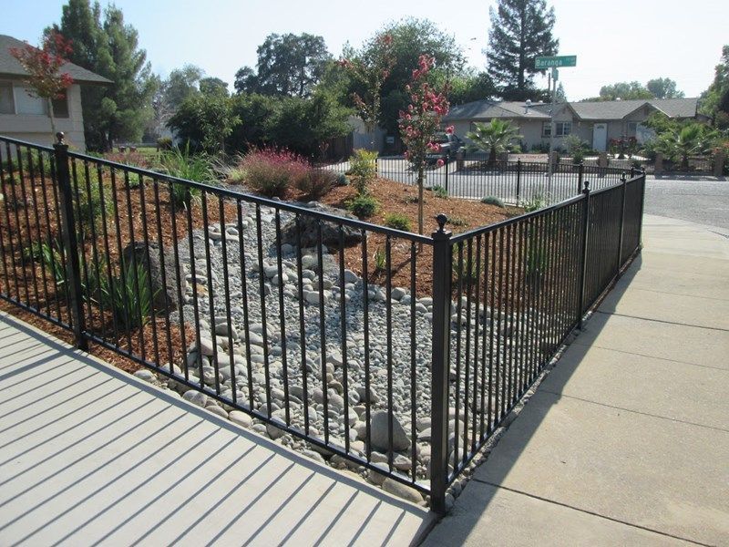A wrought iron fence surrounds a gravel area in front of a house