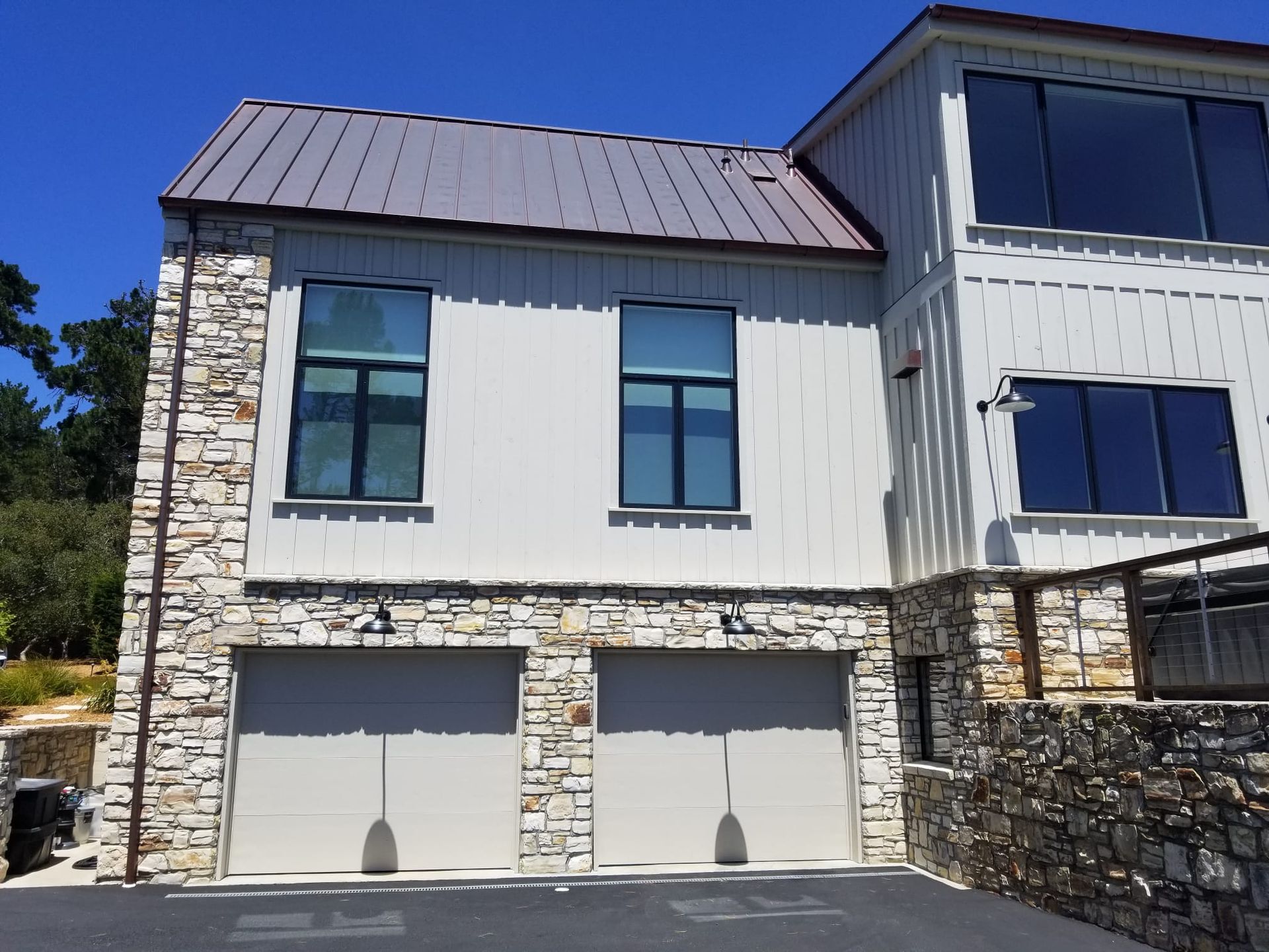 Modern house exterior with stone accents, white siding, large windows, and two garage doors under a metal roof