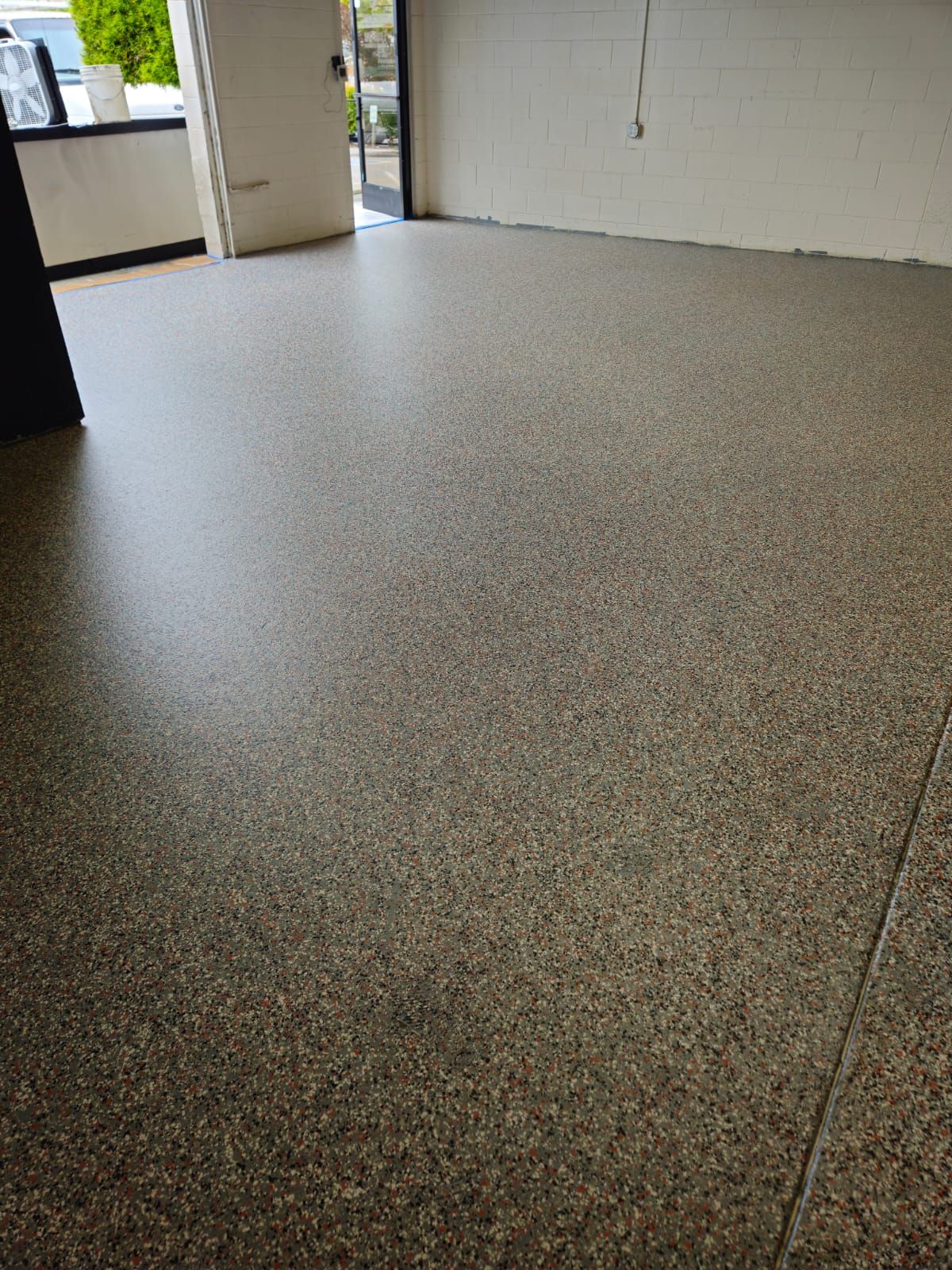 Empty room with speckled gray floor and white walls, lit by daylight from an open doorway.