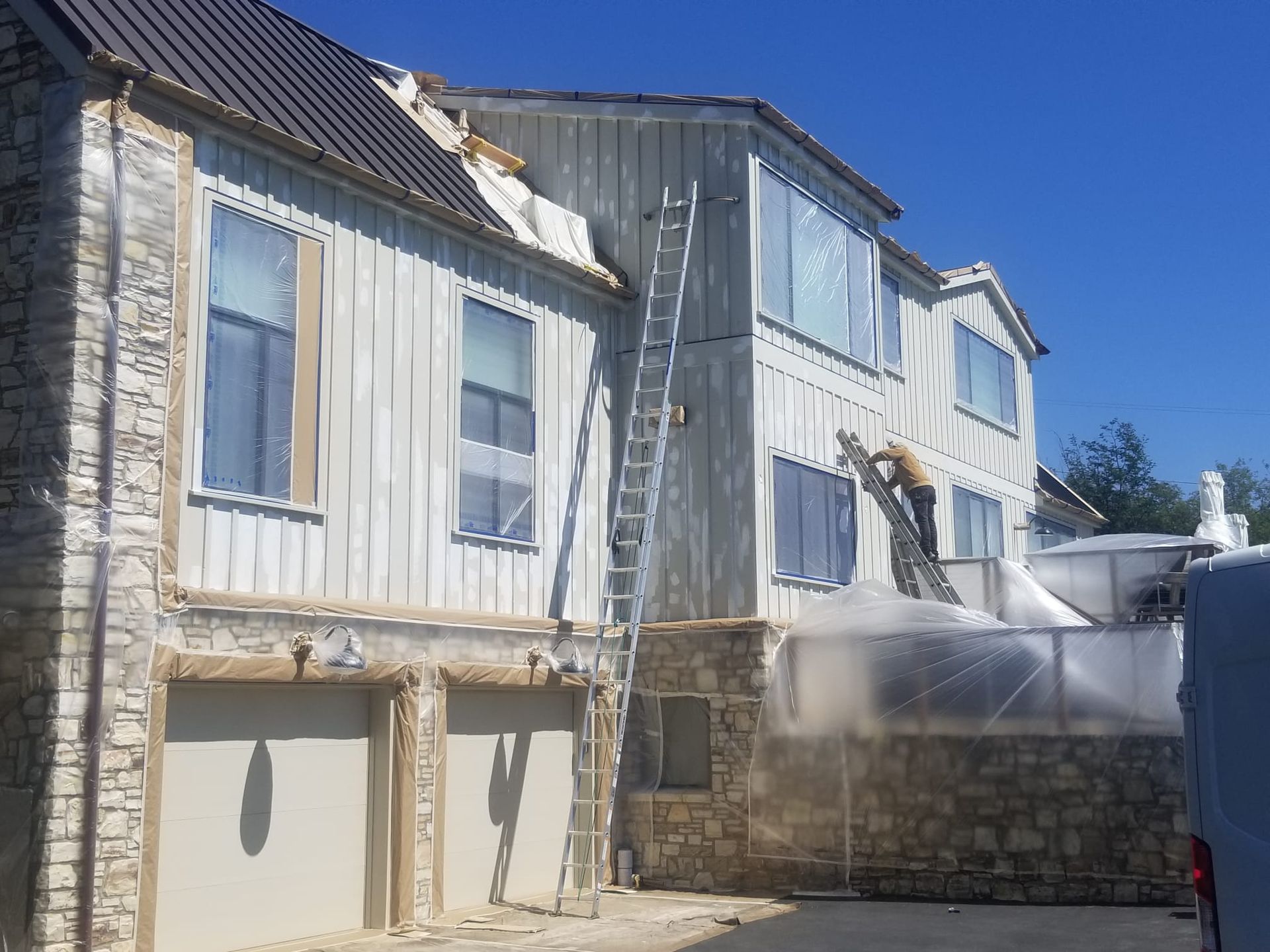 White multi-story house with damaged siding and rooftop under bright blue sky