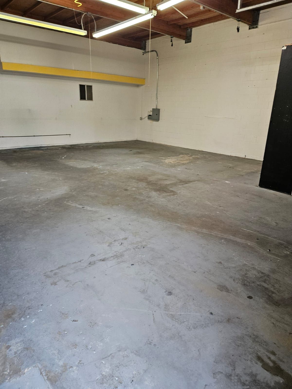 Empty concrete-floored warehouse interior with white cinderblock walls and exposed ceiling beams