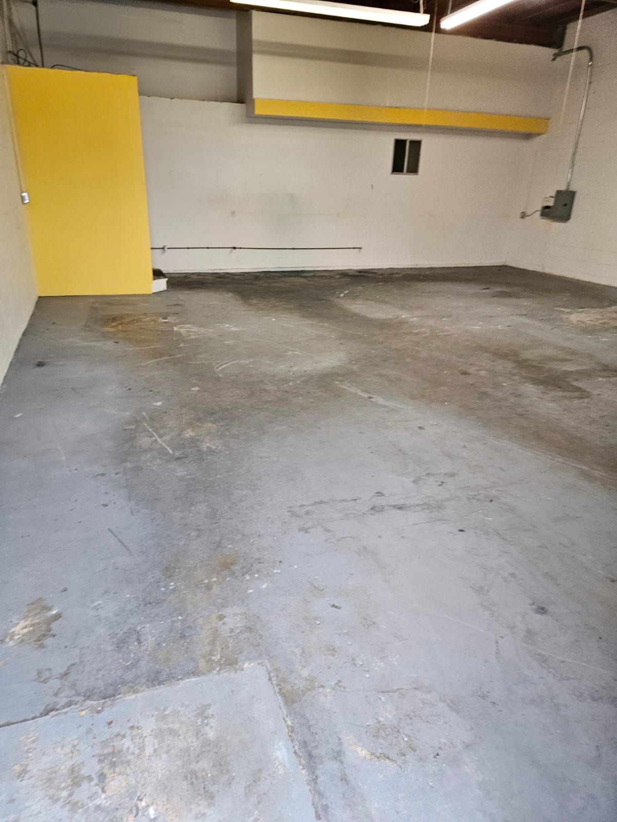 Empty concrete garage with yellow wall accents and overhead storage shelf