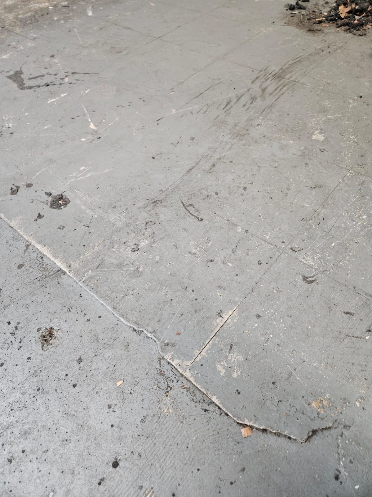 Close-up of cracked gray concrete pavement with dirt and debris scattered across it