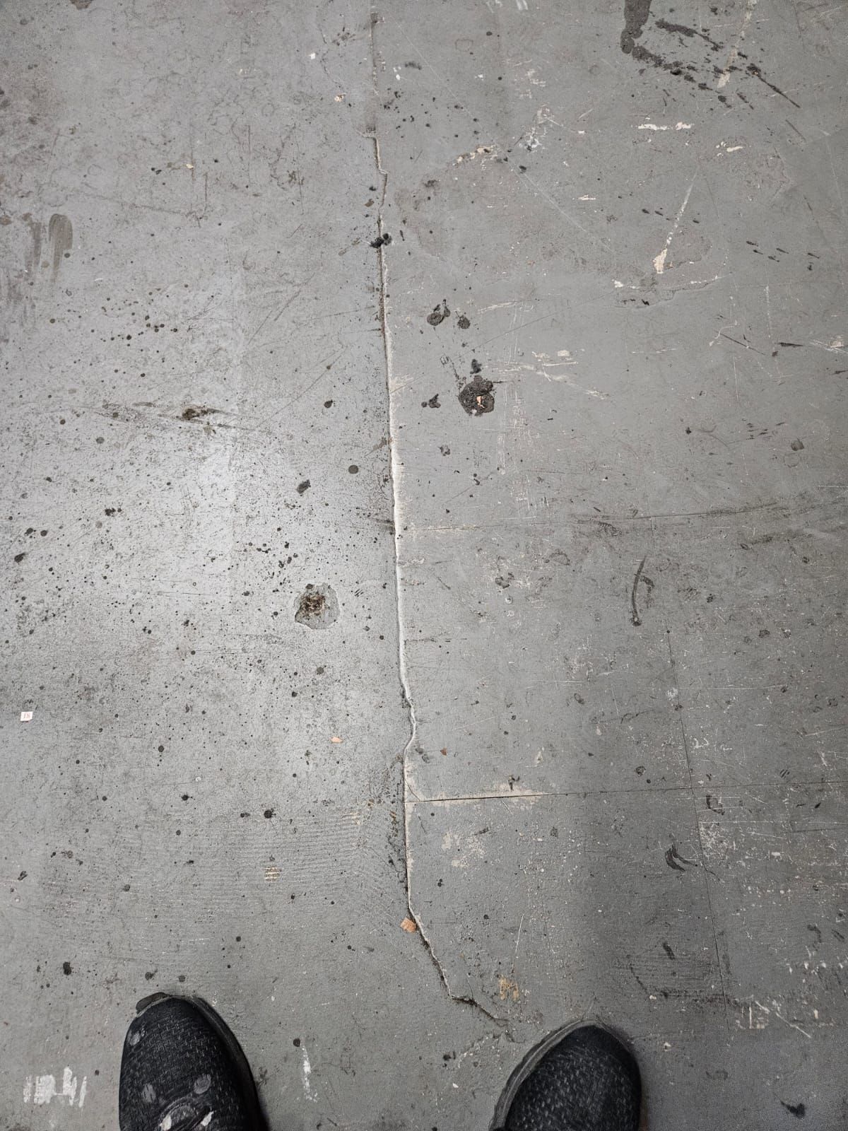 Concrete sidewalk with cracks and stains, with the tips of black shoes visible at the bottom.