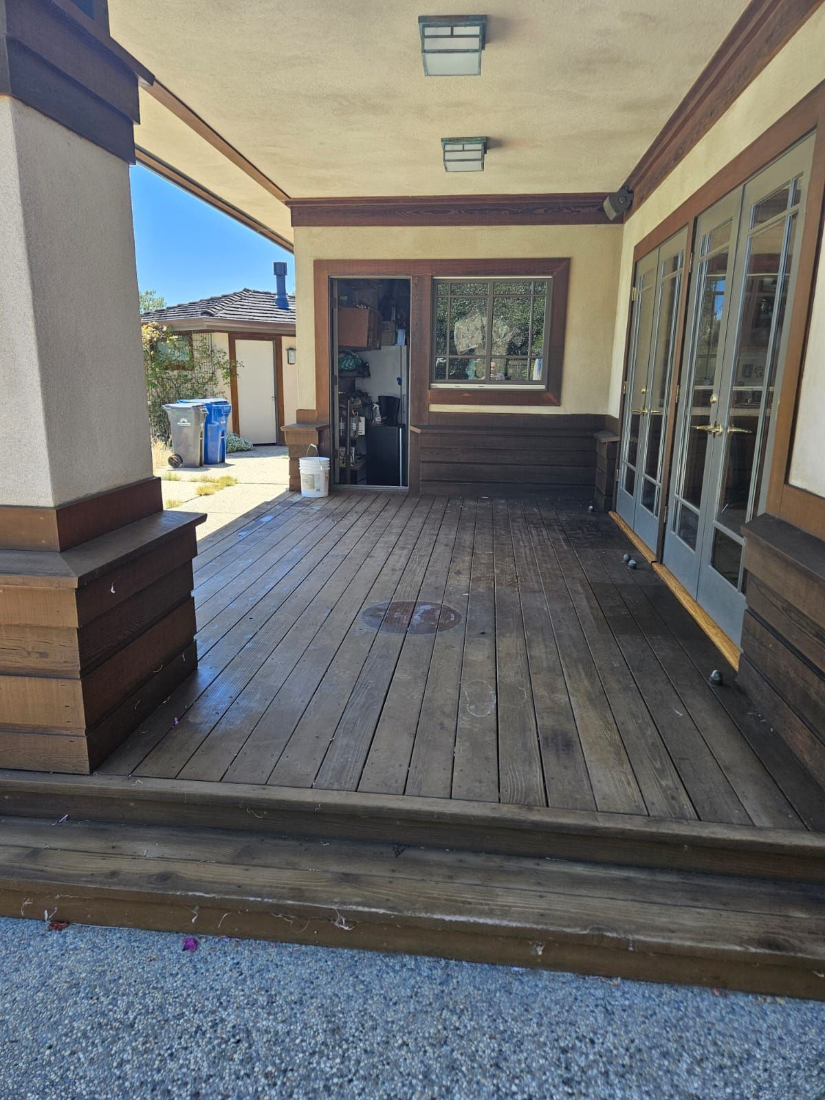 Covered wooden porch with steps, columns, and glass doors in a residential setting