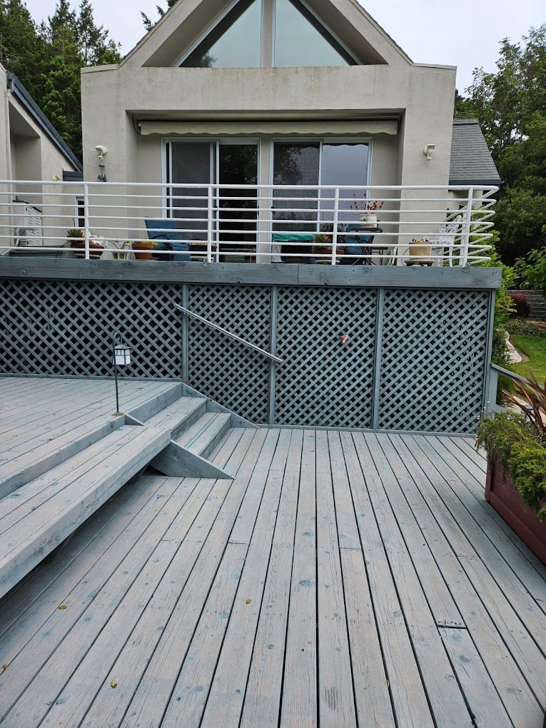 Modern house deck with gray boards, white railing, and a wide staircase leading to a patio.