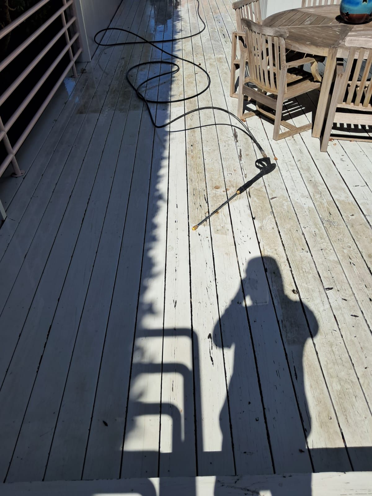 Deck with sunlit and shaded boards, a hose on the floor, and a table with chairs at the top right.