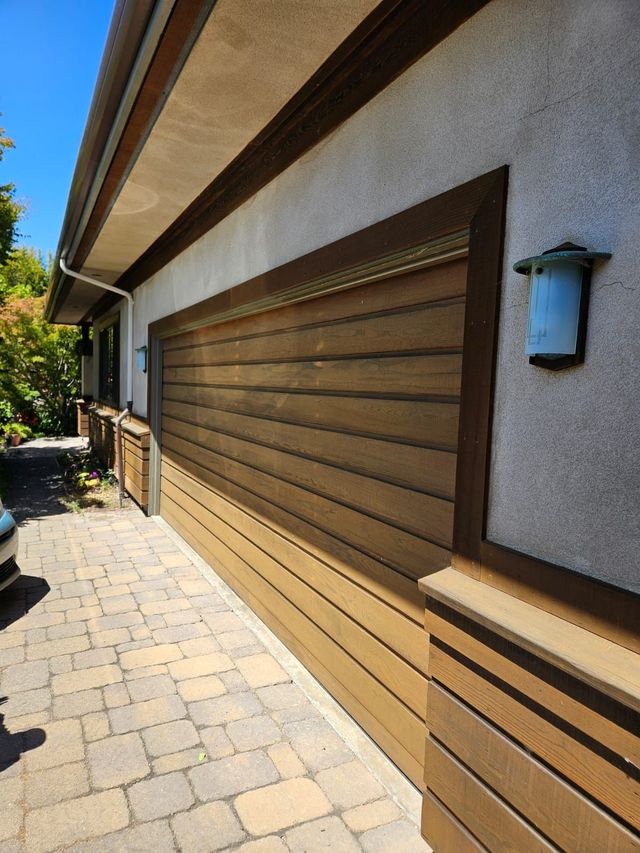 Outdoor patio beside a house with beige stucco walls, a large brown shuttered window, and stone pavers.