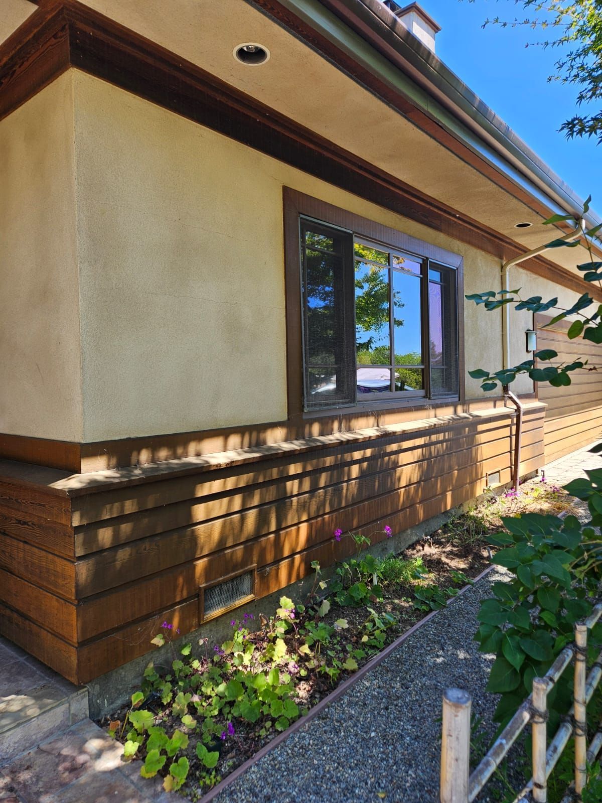 Modern house exterior with tan stucco walls, wood siding, and a window beside a garden path