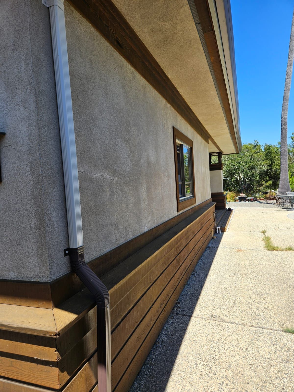 Side view of a building exterior with tan siding, windows, and a concrete walkway beside it
