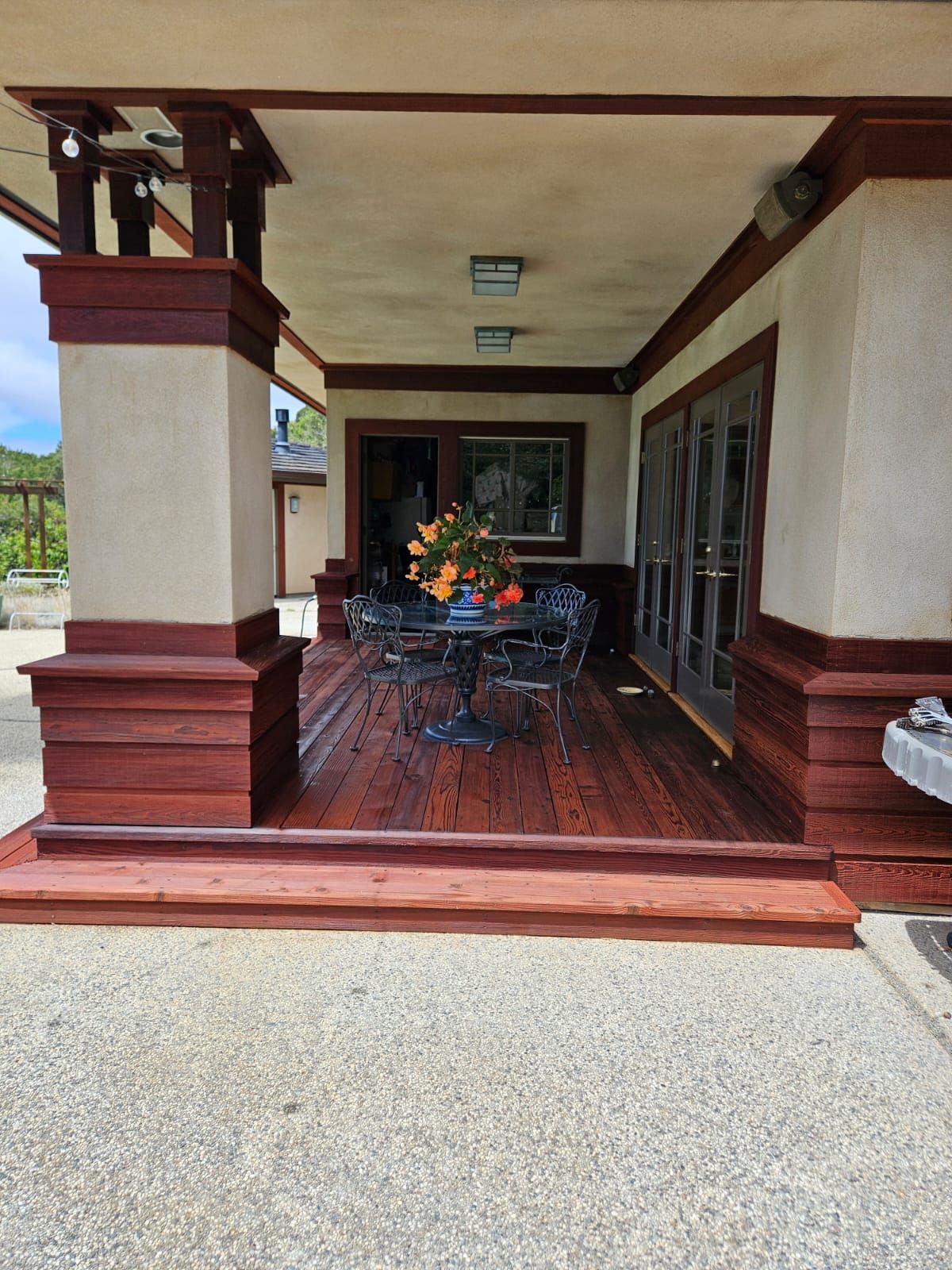Covered front porch with wooden floor, columns, and a patio table with flowers and chairs.