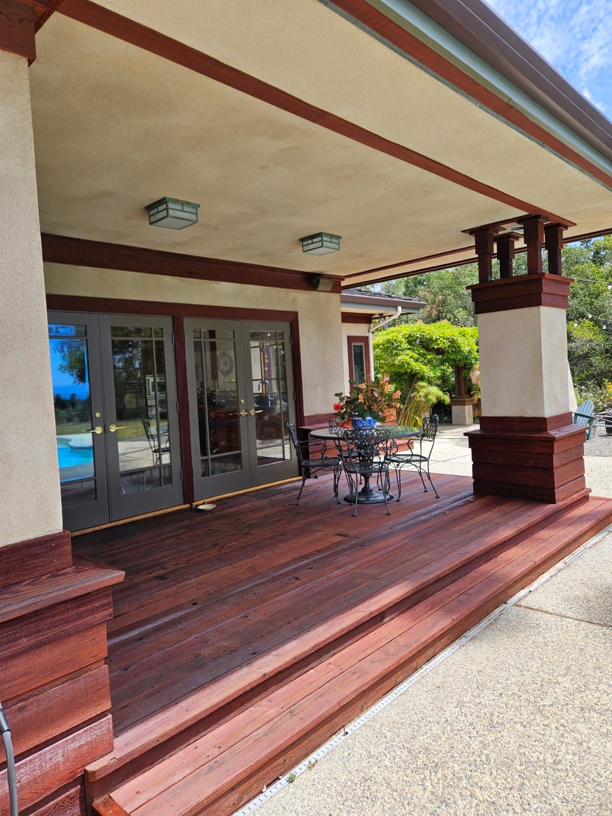 Covered porch with redwood deck, glass doors, and small patio table and chairs outside a building