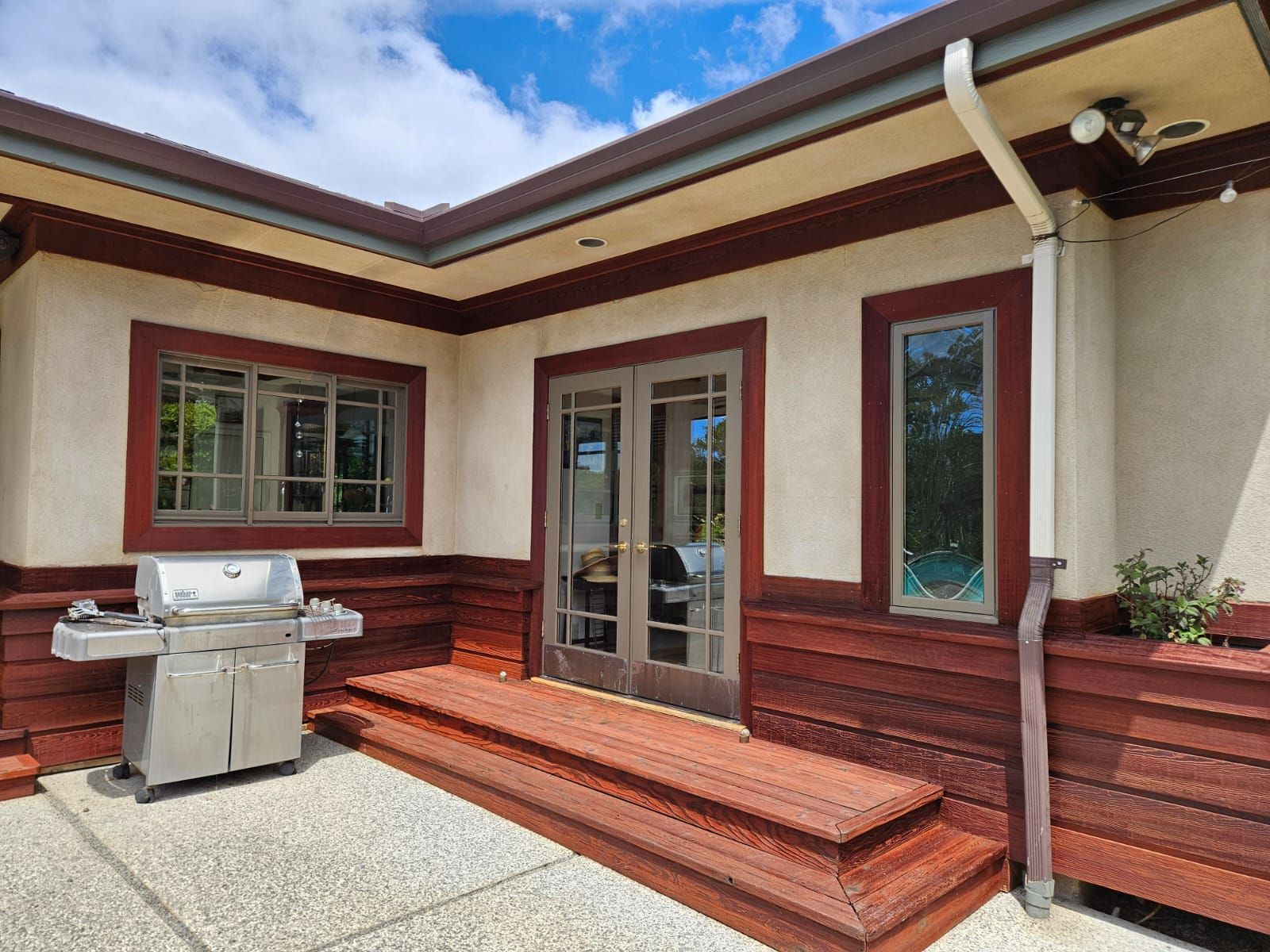 Patio with wood steps, glass doors, windows, and a stainless steel grill outside a house