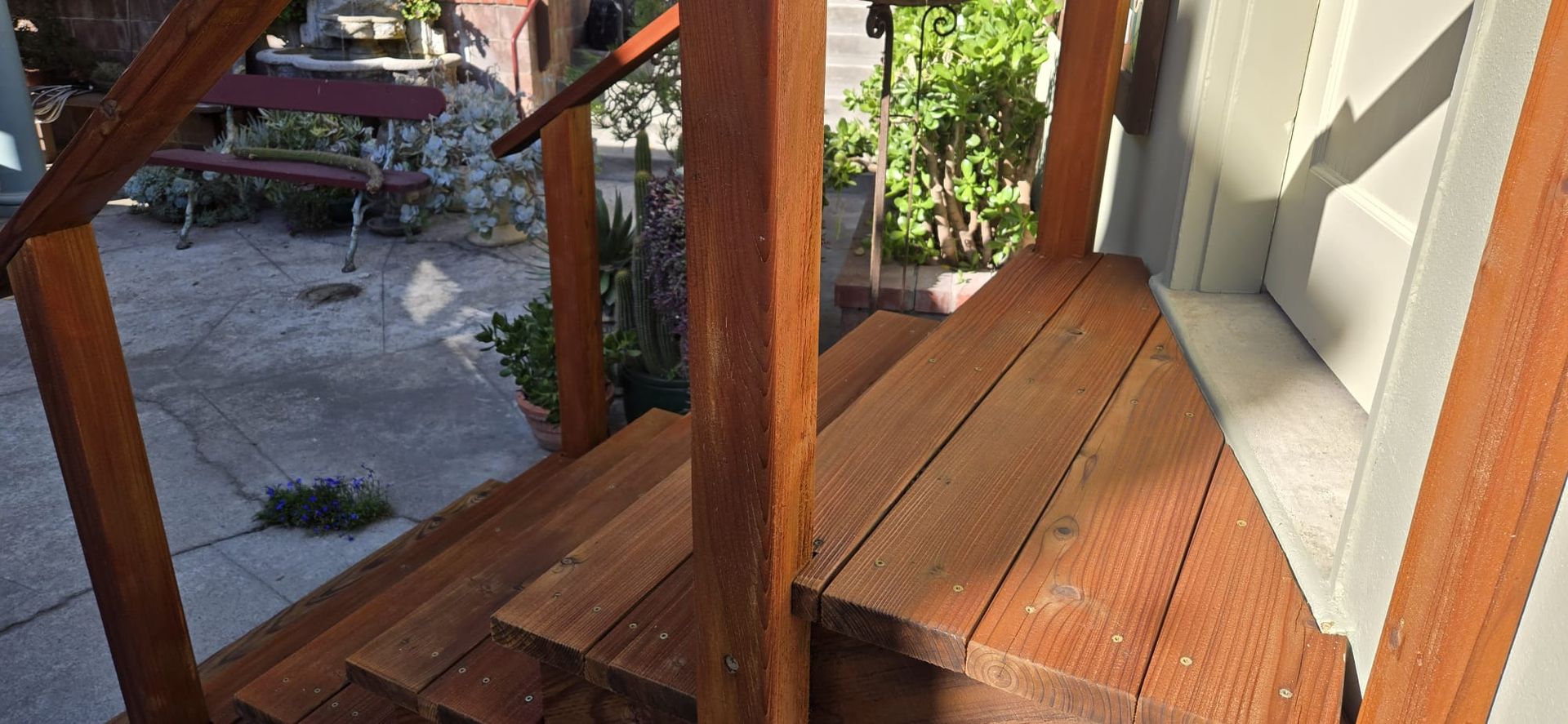 Wooden porch stairs beside a house, overlooking a garden path and greenery.
