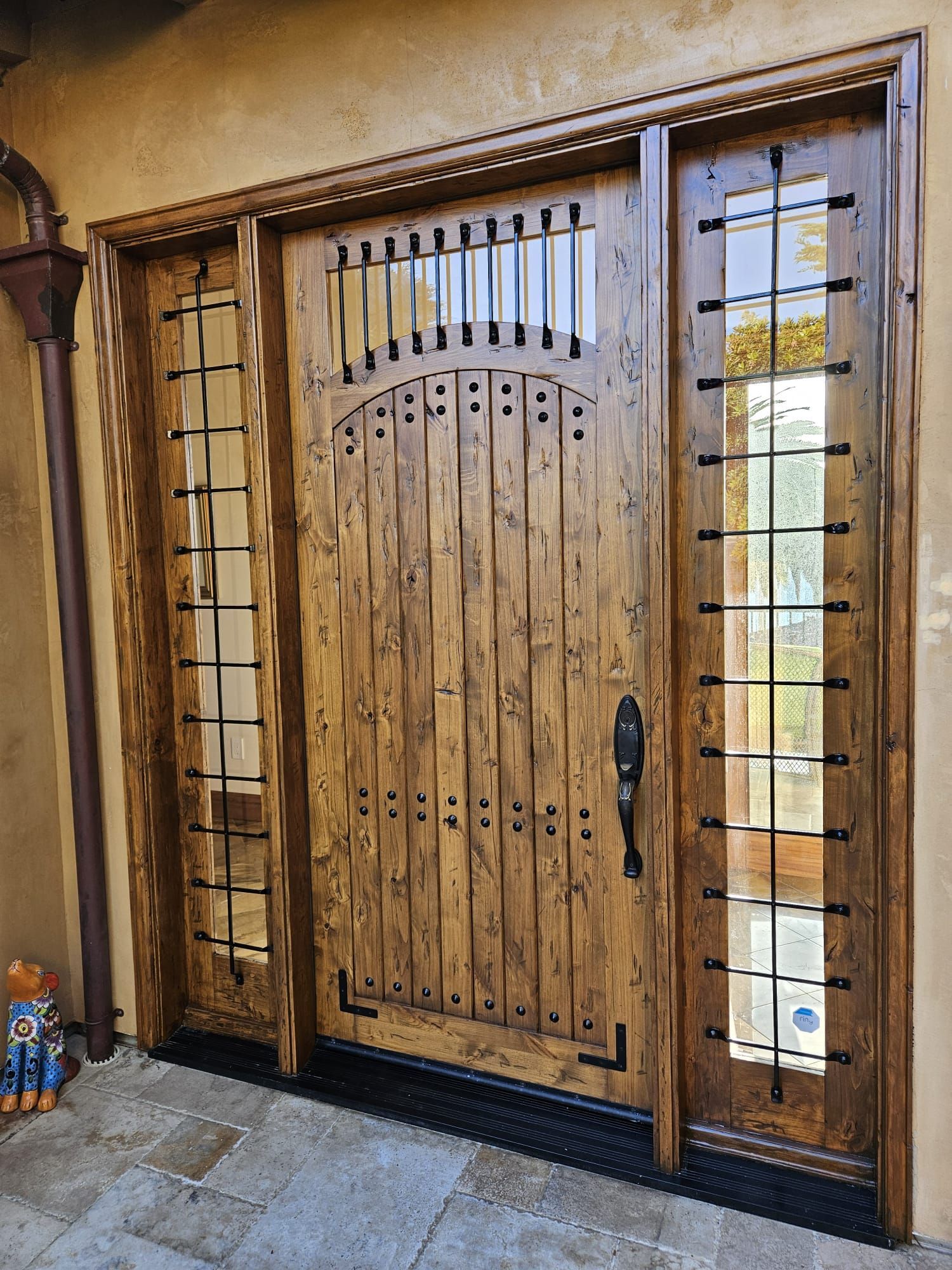 Wooden front door with decorative glass panels and black metal handle in a stone entryway