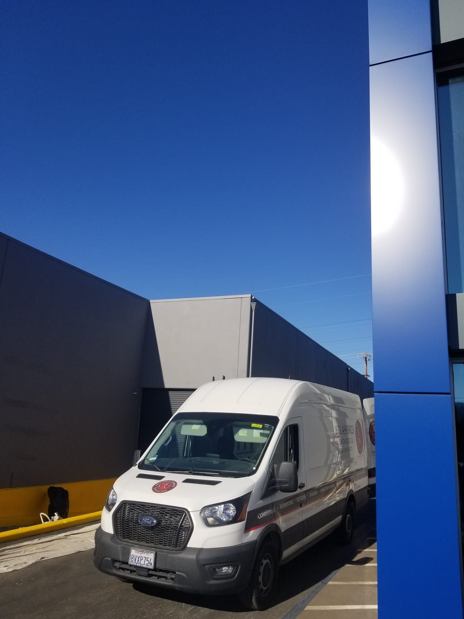 White delivery van parked beside a blue building in a sunny industrial alley