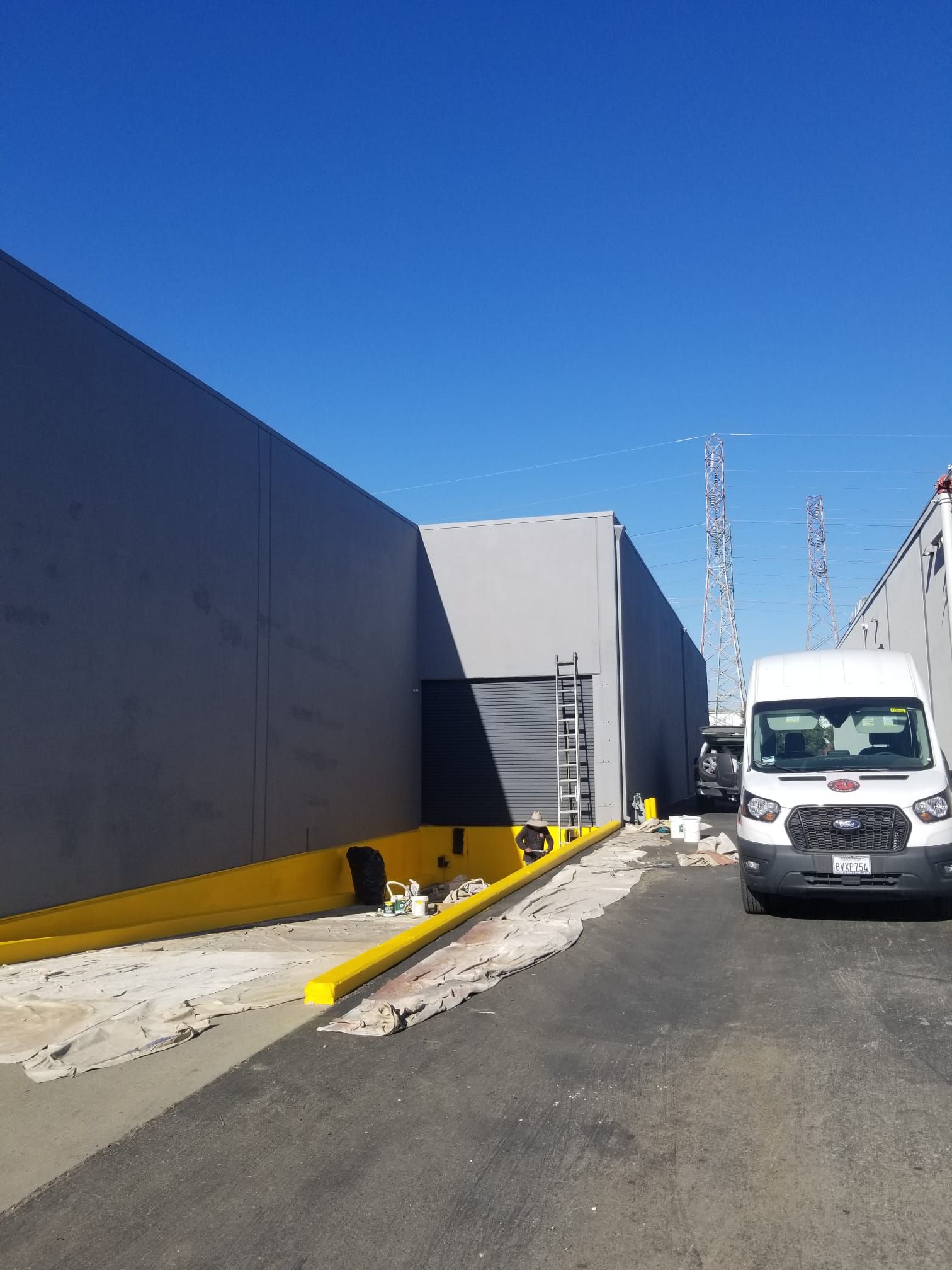 Industrial warehouse alley with a white van parked beside gray buildings under a blue sky