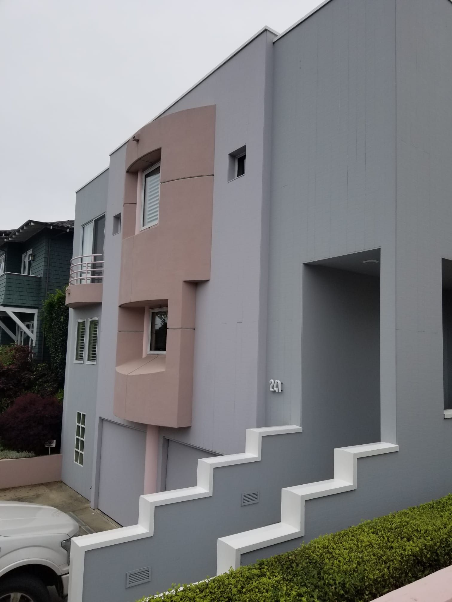 Modern townhouse exterior with gray and pink facade, stepped front wall, and small windows
