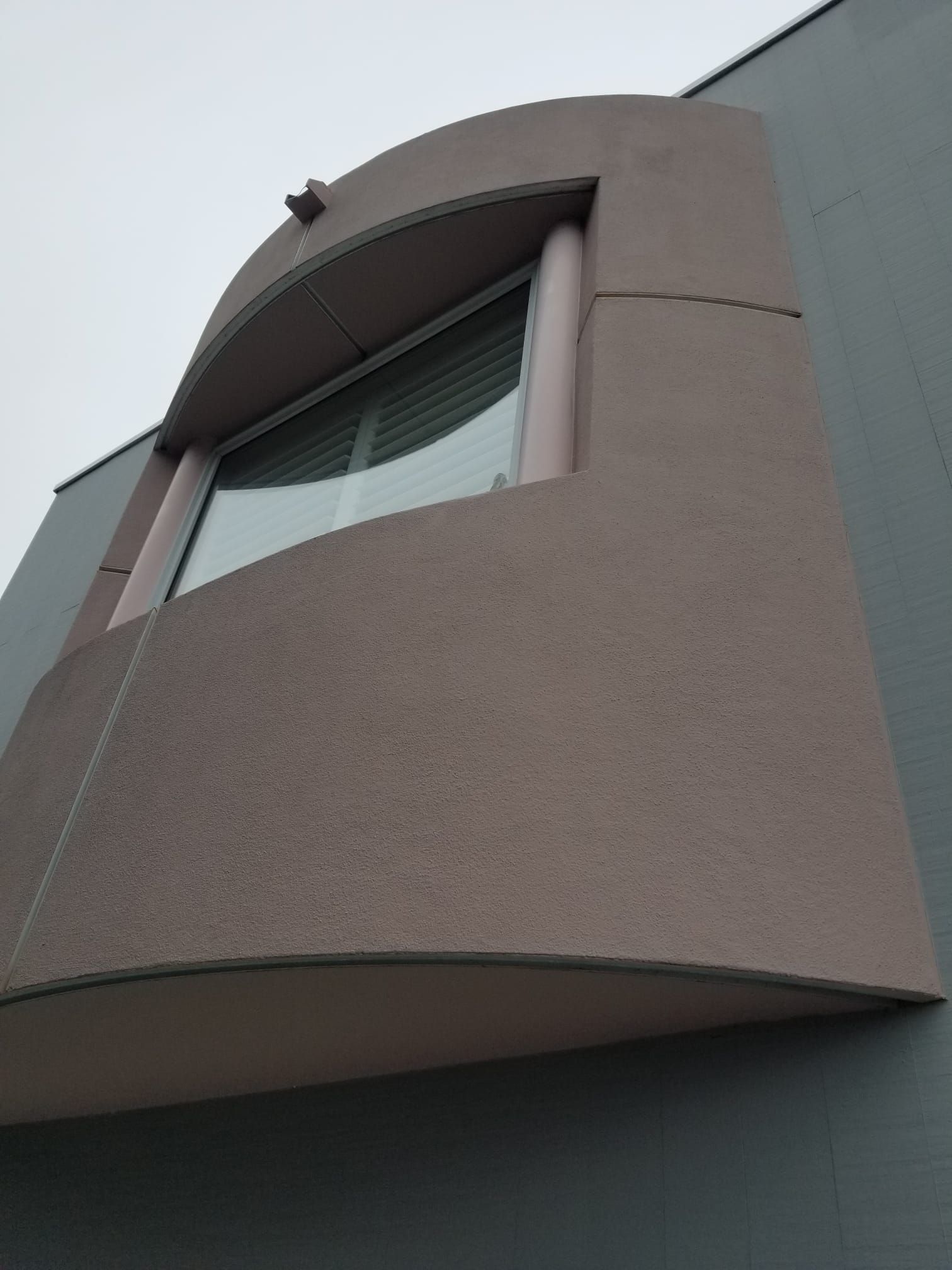 Low-angle view of a modern building facade with a curved brown balcony and window