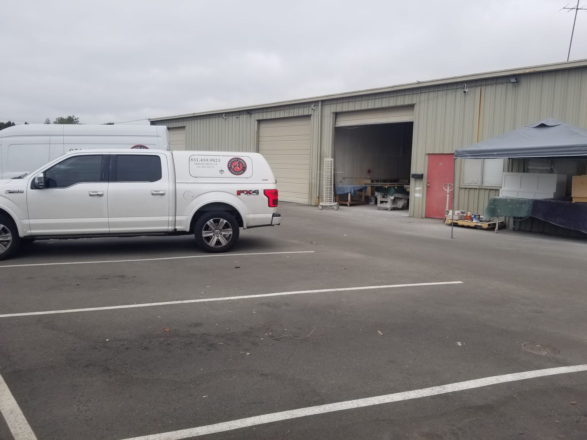 White pickup truck parked outside a warehouse with open garage doors and a canopy in the lot.