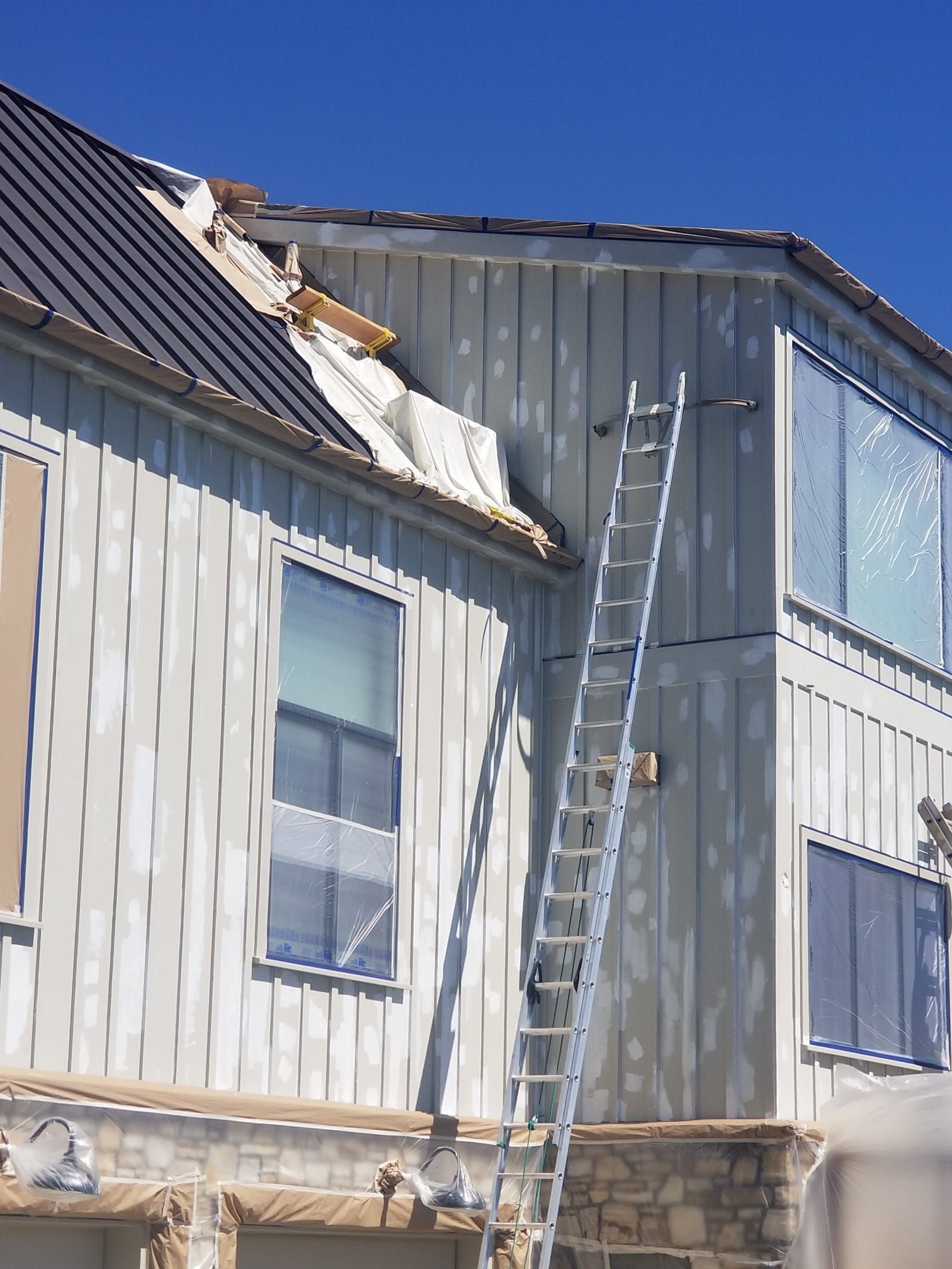 Damaged house exterior with a ladder leaning against the upper wall and roof damage visible