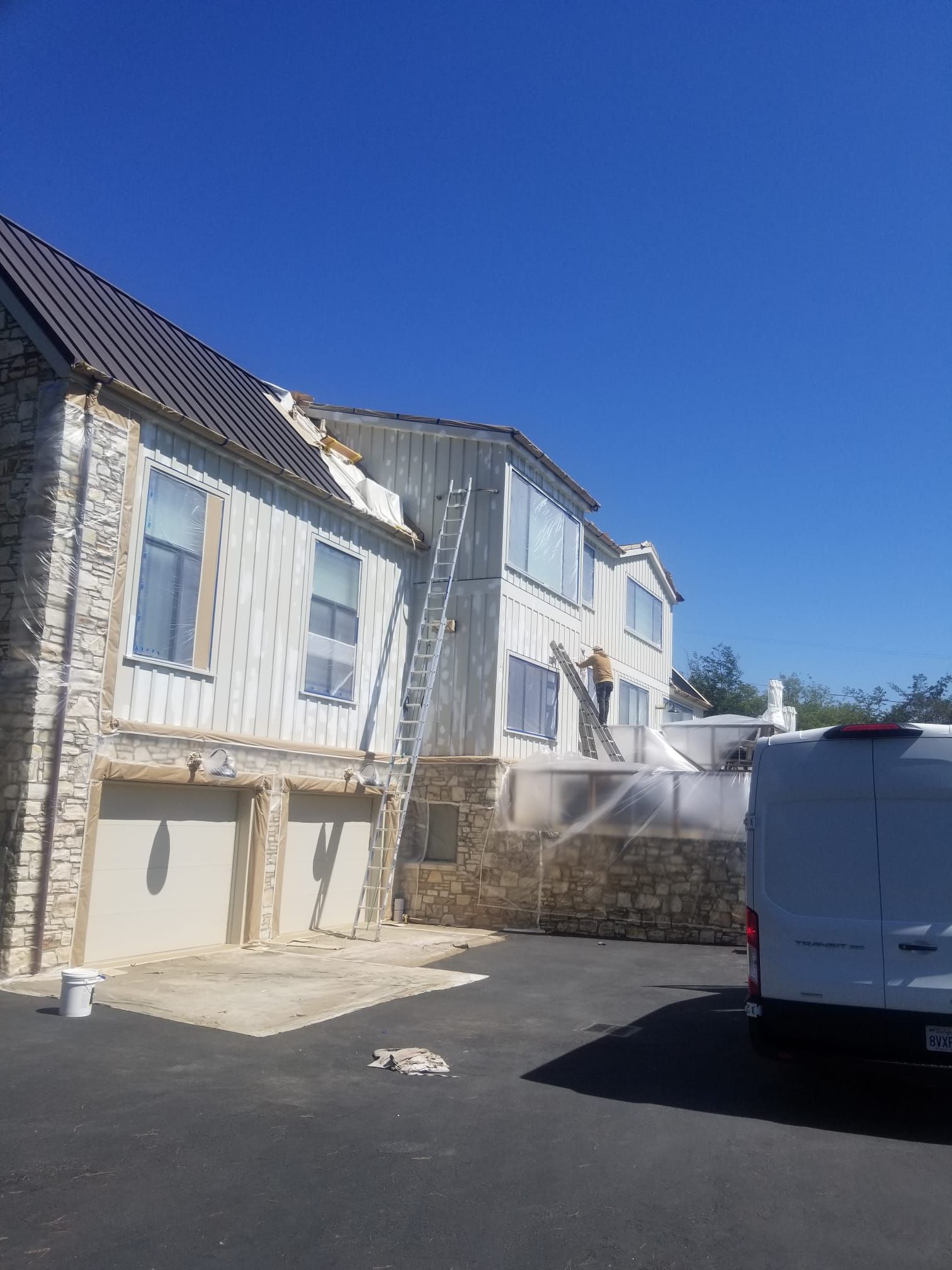 White residential building with sunlit balconies and a parked white van in a driveway under a clear blue sky