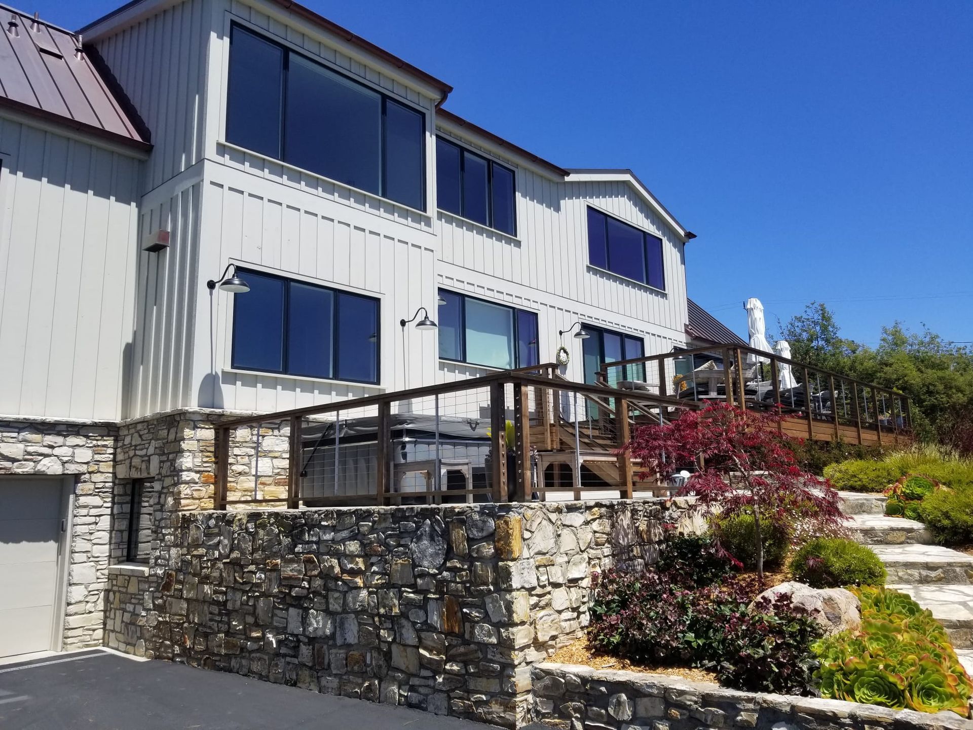 Modern house with stone terrace, railing, and landscaped garden under a blue sky