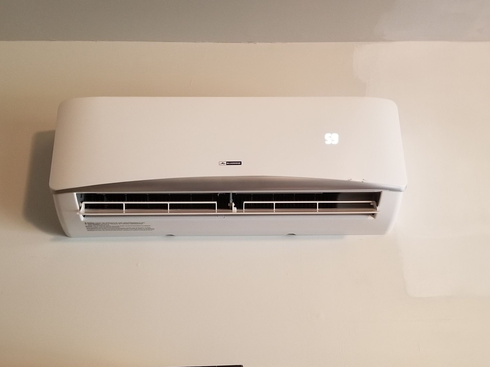 A white air conditioner is hanging on a white wall.