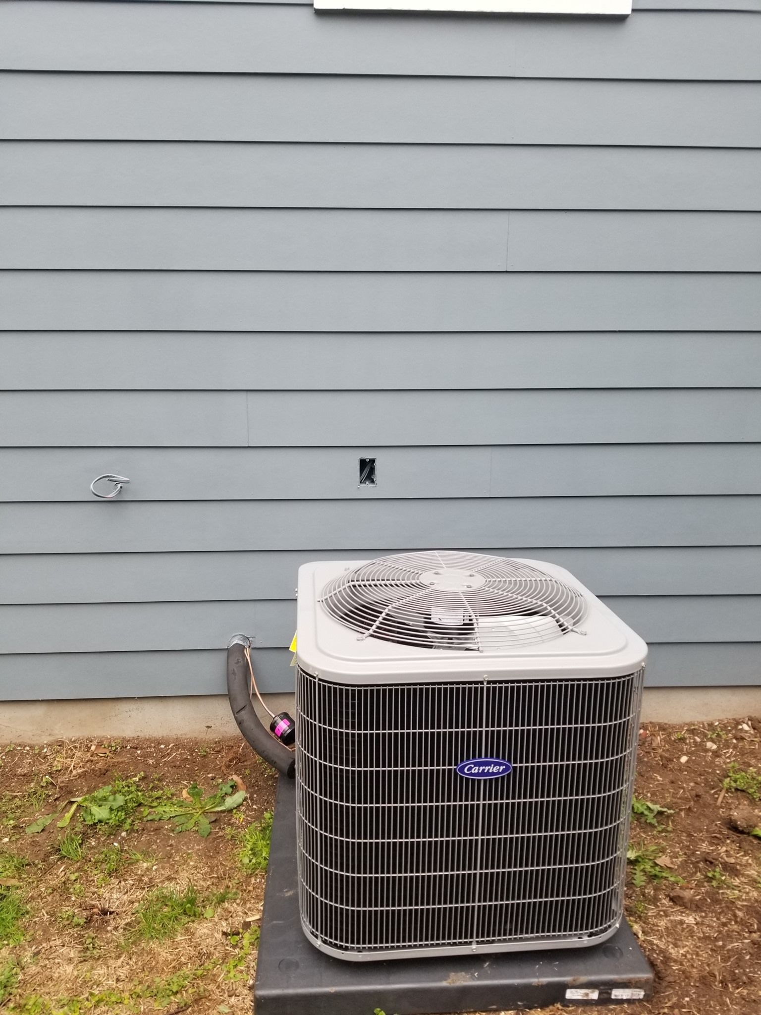 A carrier air conditioner is sitting outside of a house.