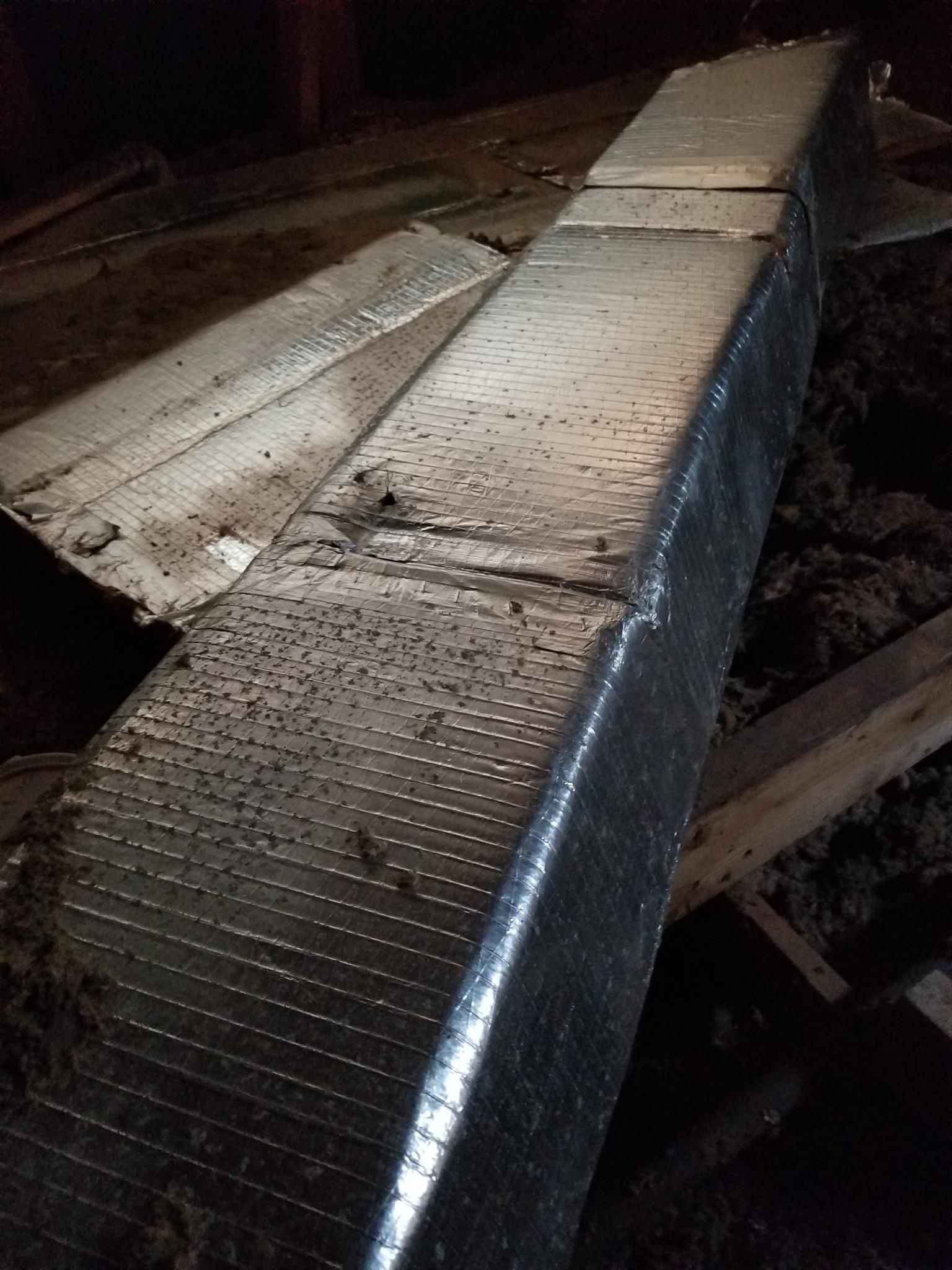 A metal pipe is sitting on top of a wooden floor in an attic.
