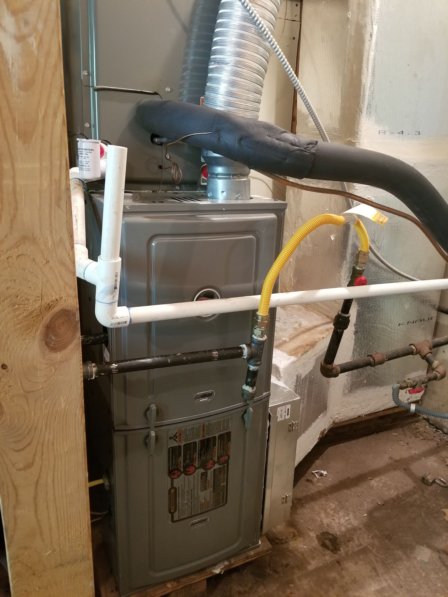 A furnace is sitting in a basement next to a wooden wall.