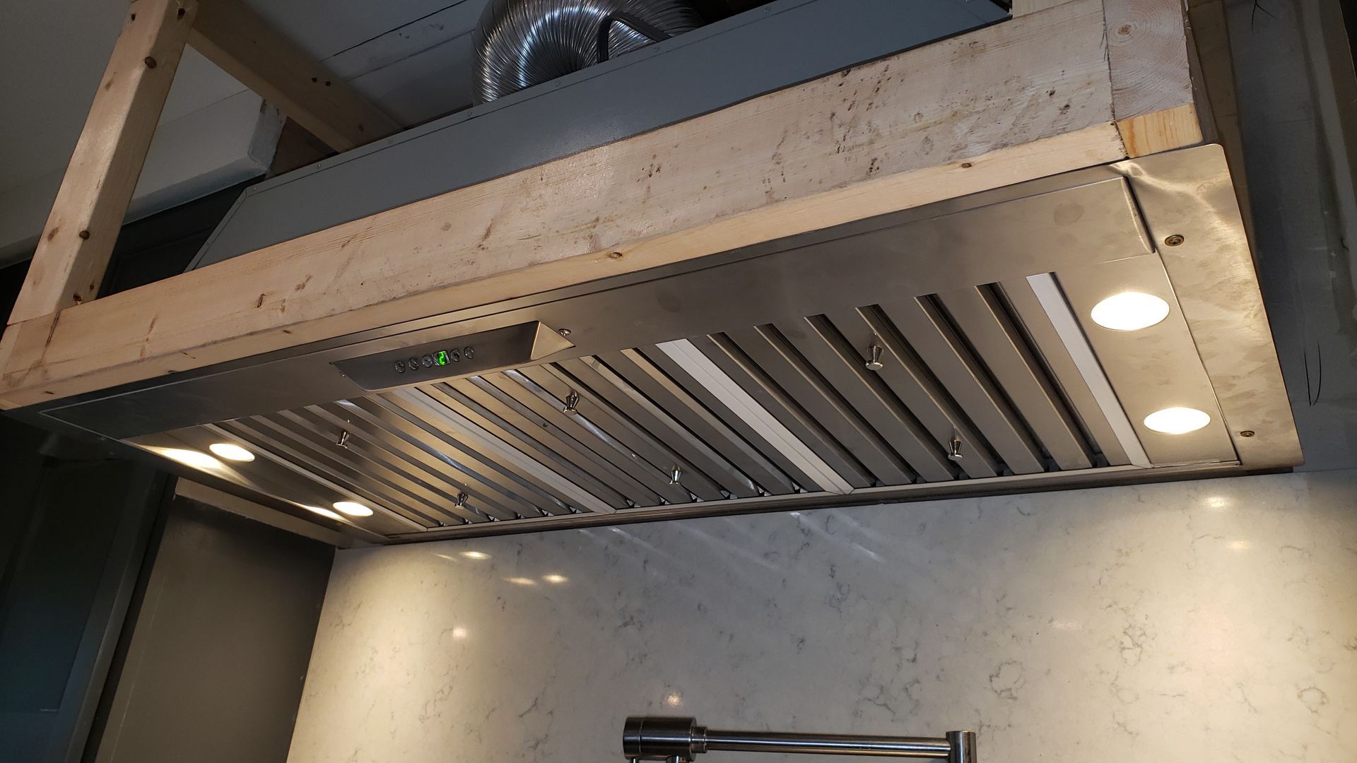 A stainless steel hood is hanging from the ceiling in a kitchen