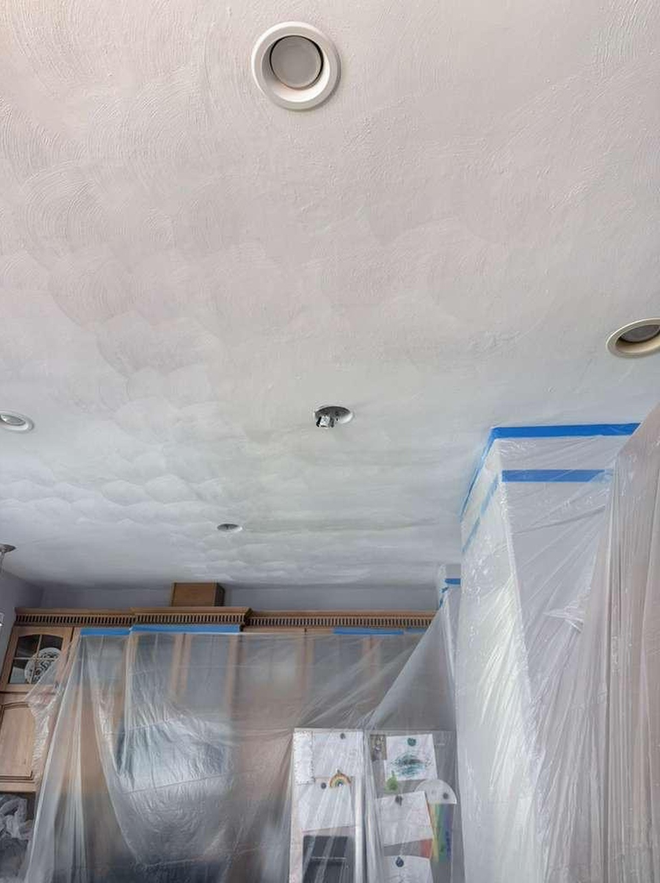 Plastic-covered room ceiling with recessed lights and a blue-taped corner during renovation