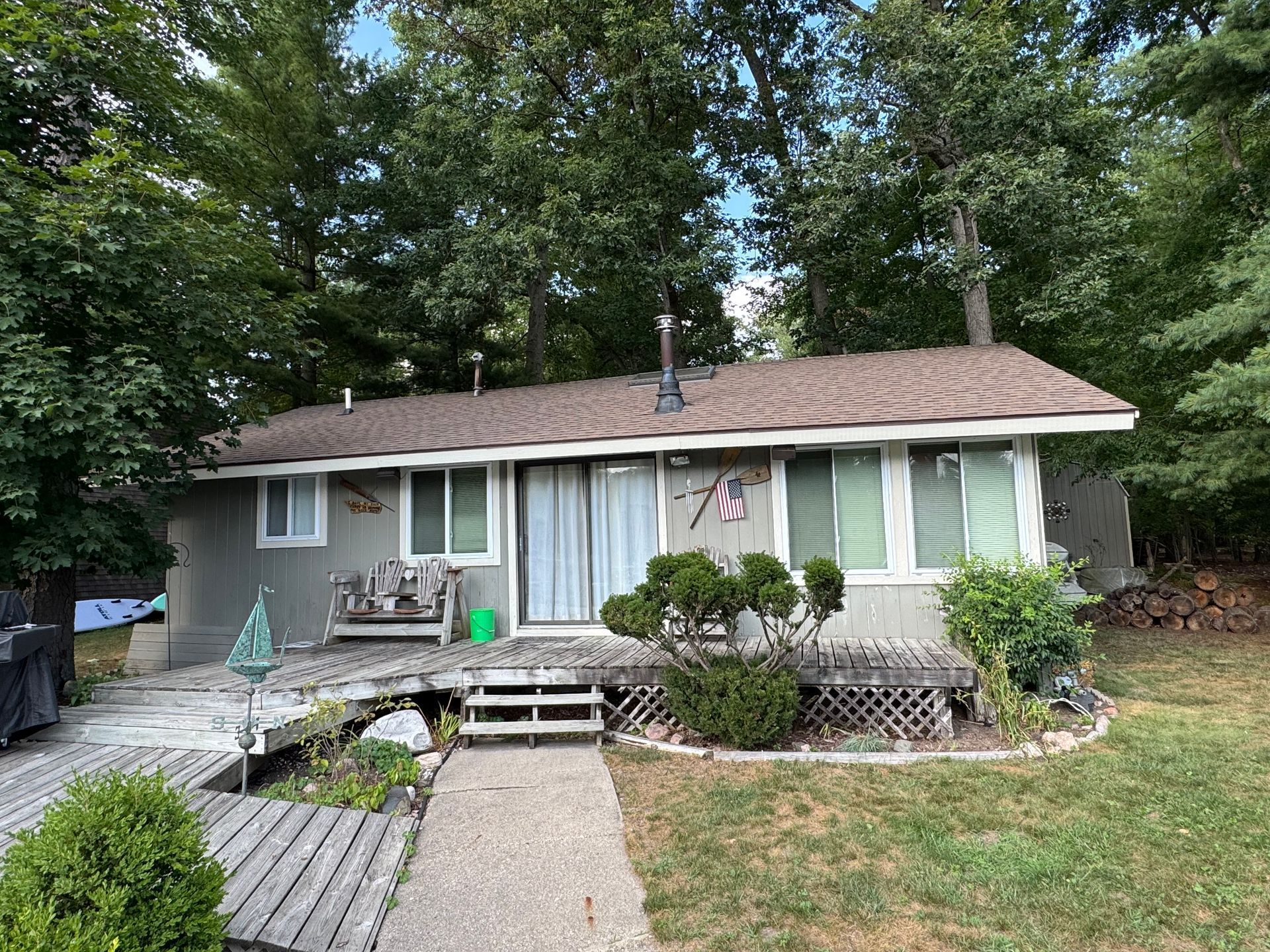 Small gray house with a front porch, steps, and a lawn surrounded by trees.