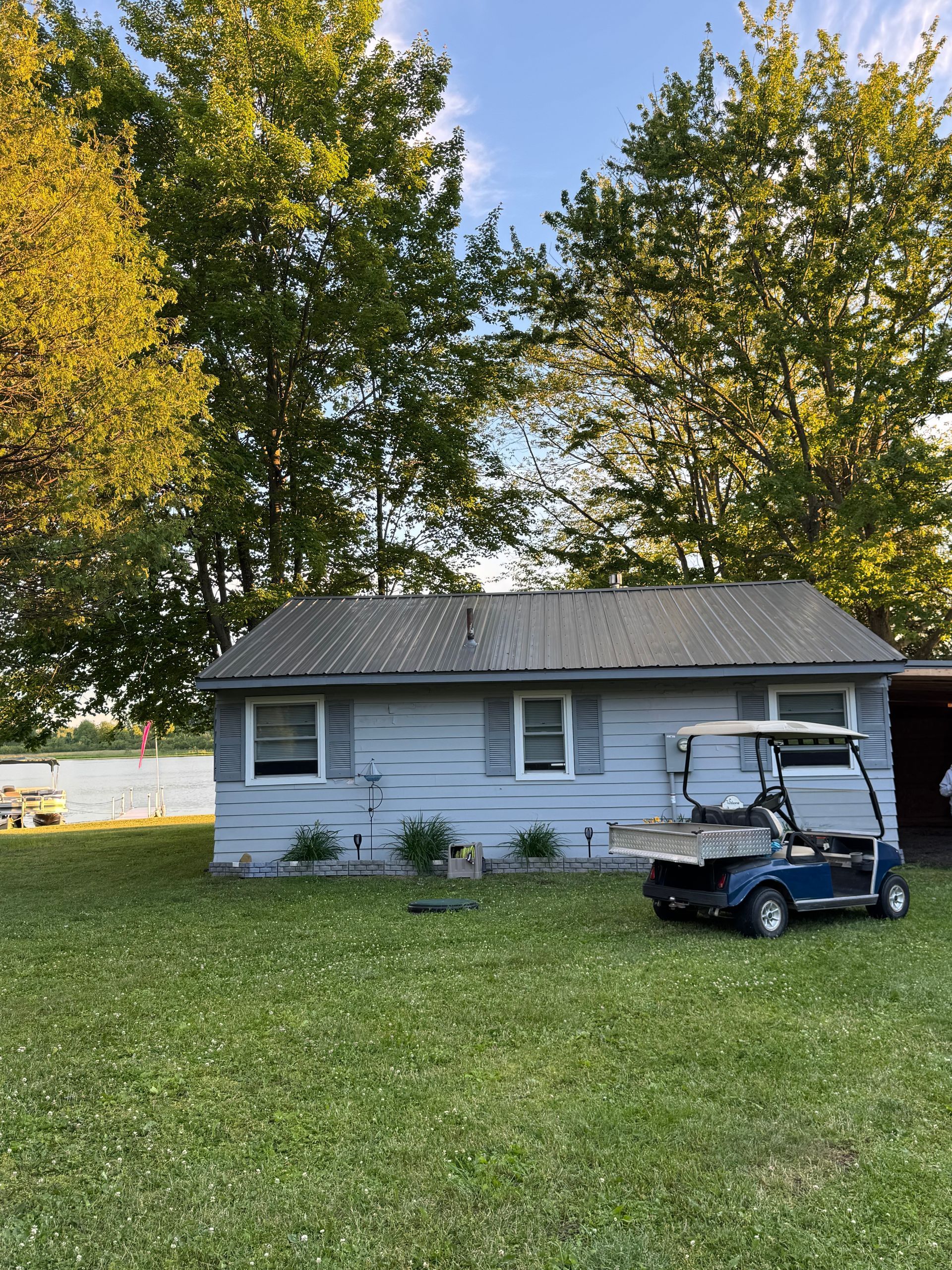 Small white house with gray roof and a golf cart in front, surrounded by trees and a grassy yard.