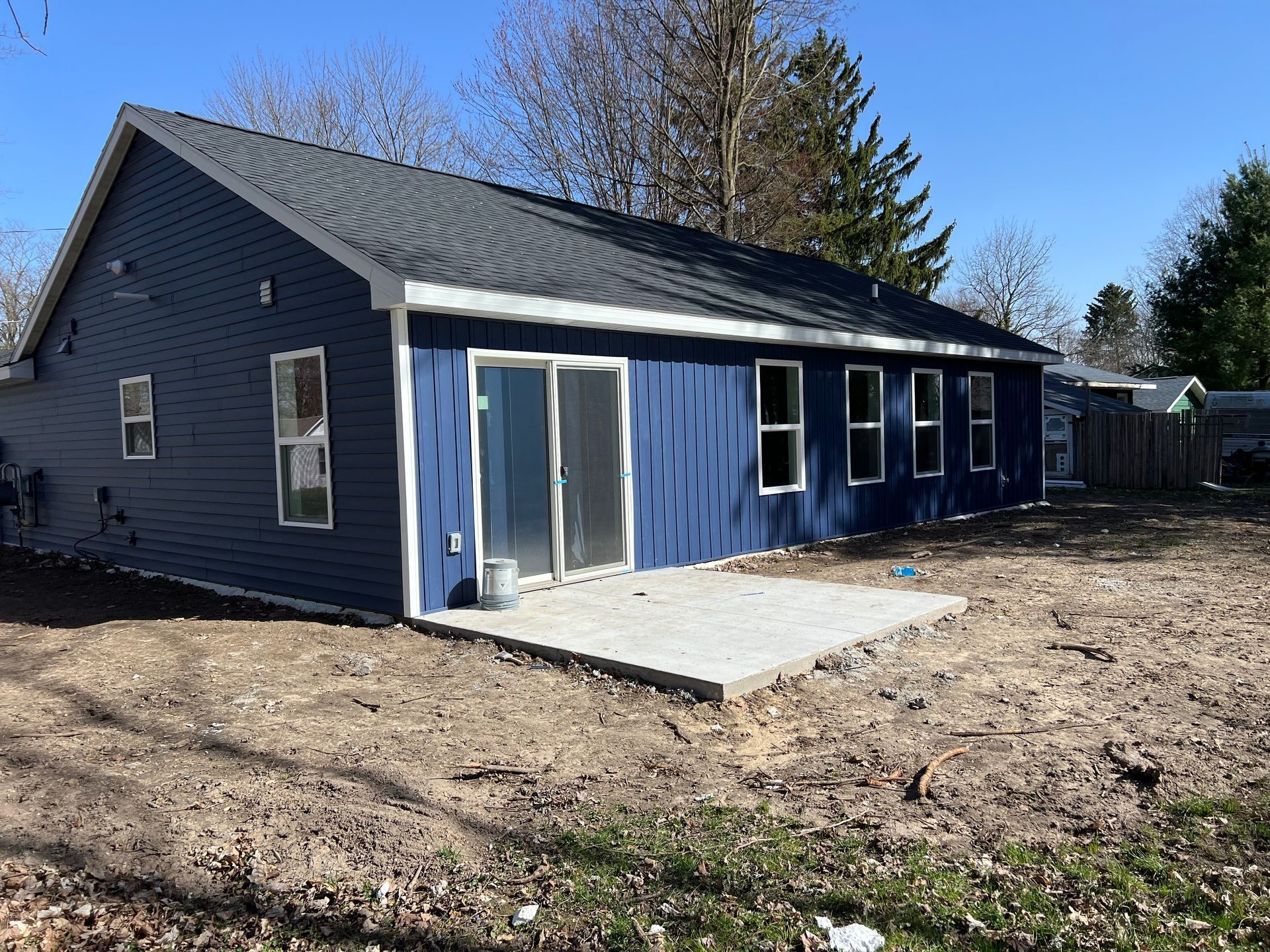 Blue single-story house with a gray roof and small concrete patio in a yard under a clear sky