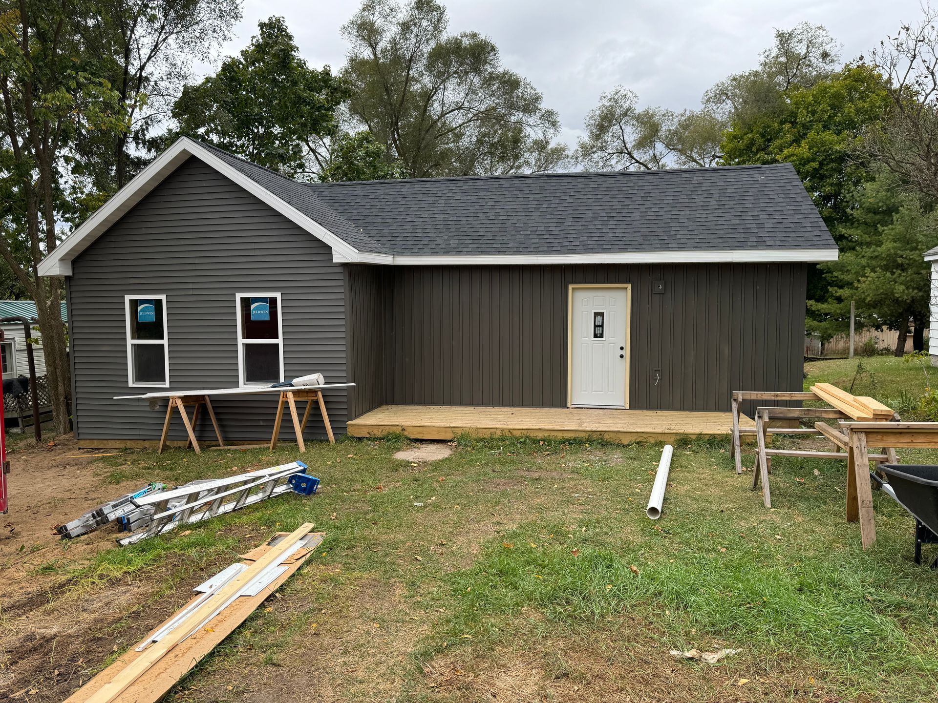 Small brown shed in a grassy yard, with tools and lumber scattered in front.