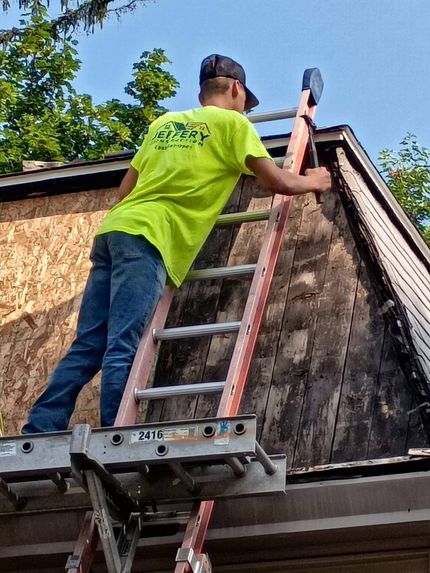 Worker on a ladder repairing the roof edge of a house outdoors.