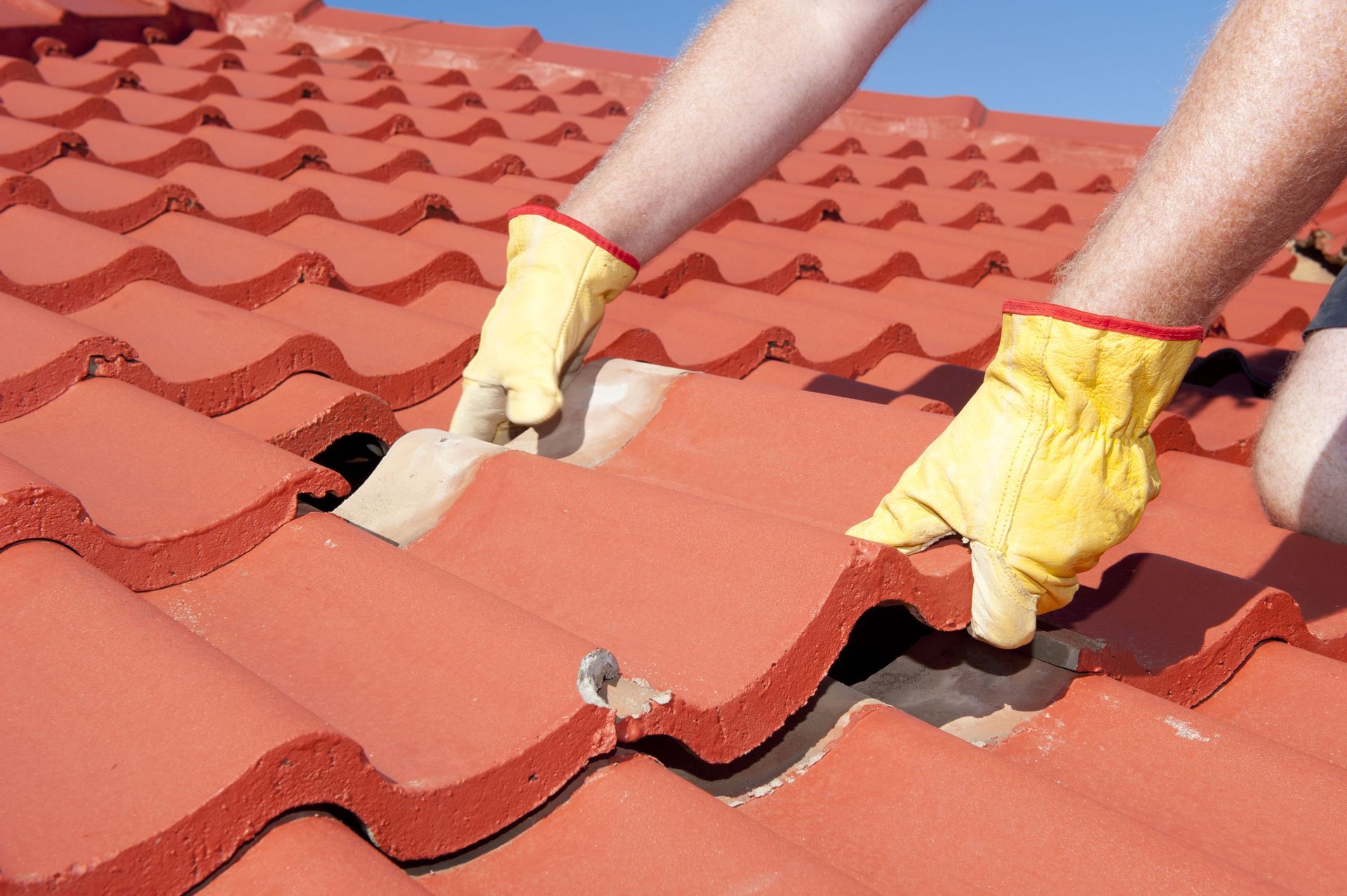Hands wearing yellow gloves installing red roof tiles on a tiled roof