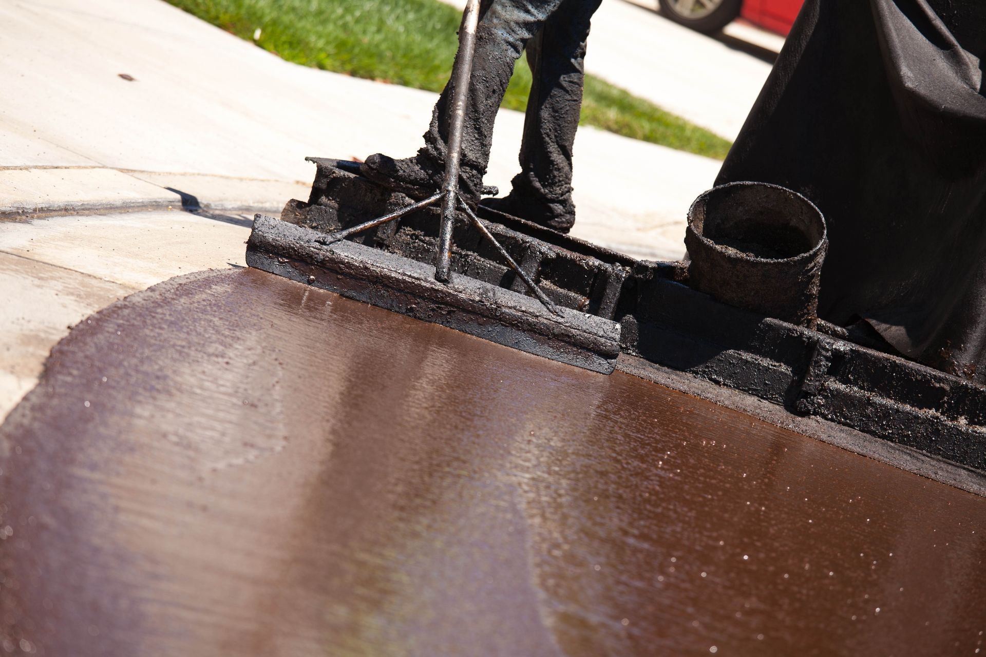 Person applying asphalt sealant to a driveway with a squeegee.