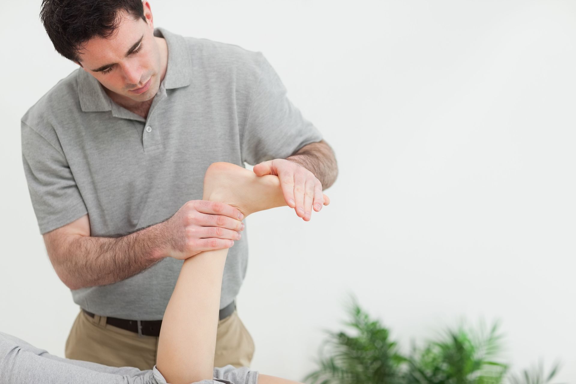 Man in gray shirt gently stretching a person’s bent arm in a bright room