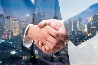 Two businessmen are shaking hands in front of a city skyline.