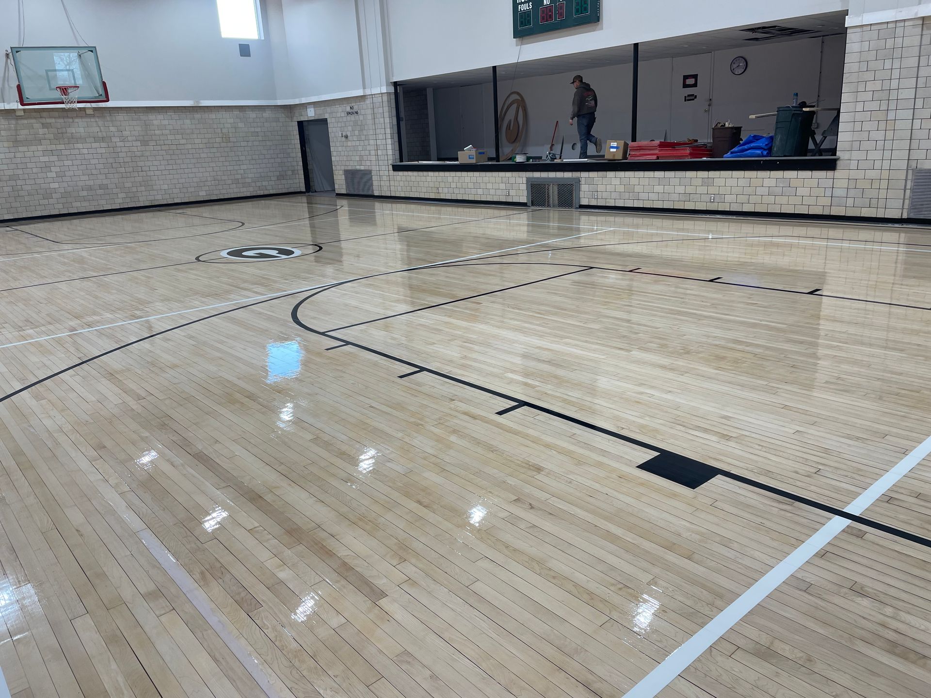 An empty gym with a wooden floor and a basketball hoop