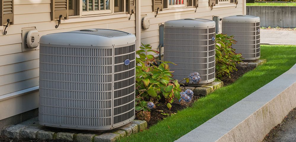 Three air conditioners are sitting on the side of a house.