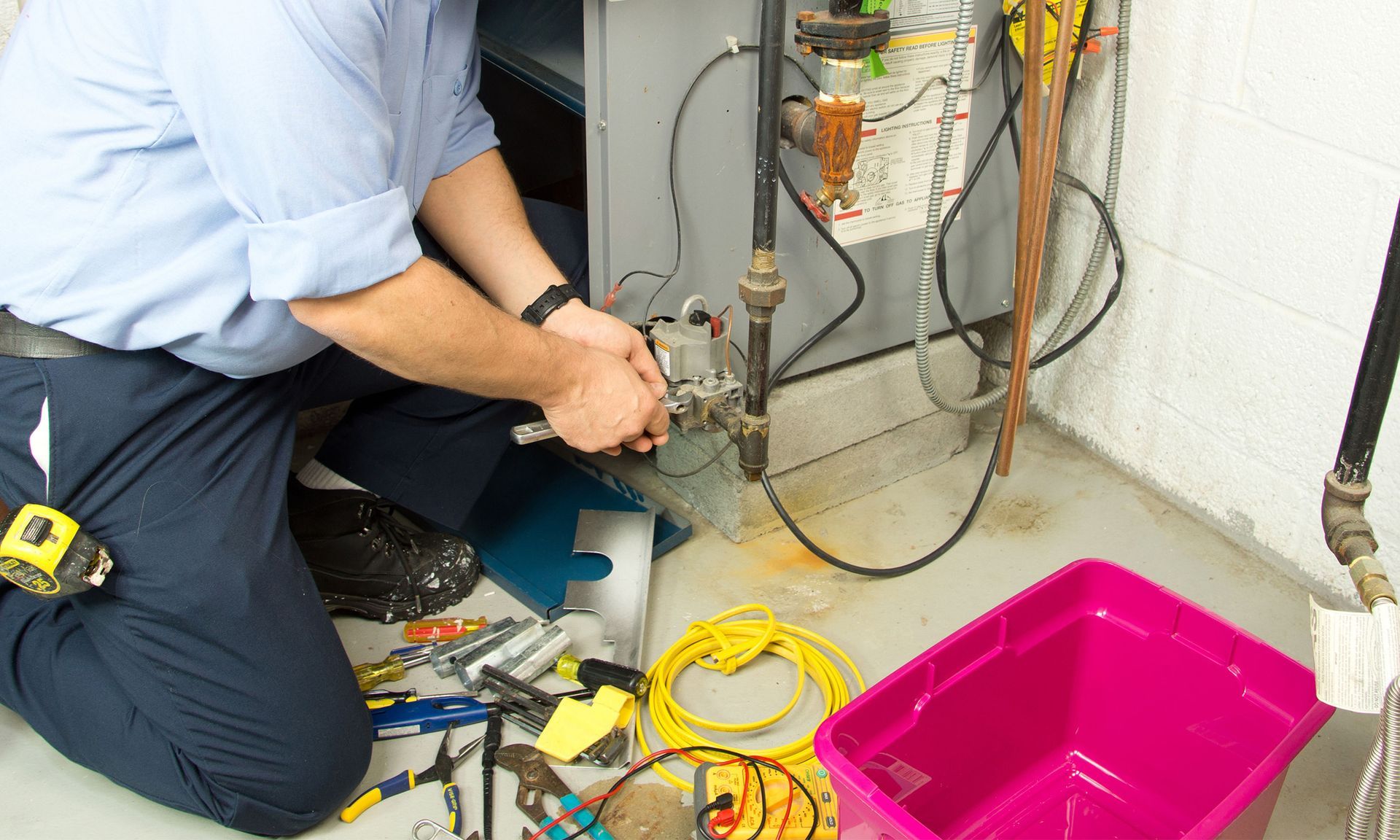 A man is kneeling on the floor fixing a water heater.