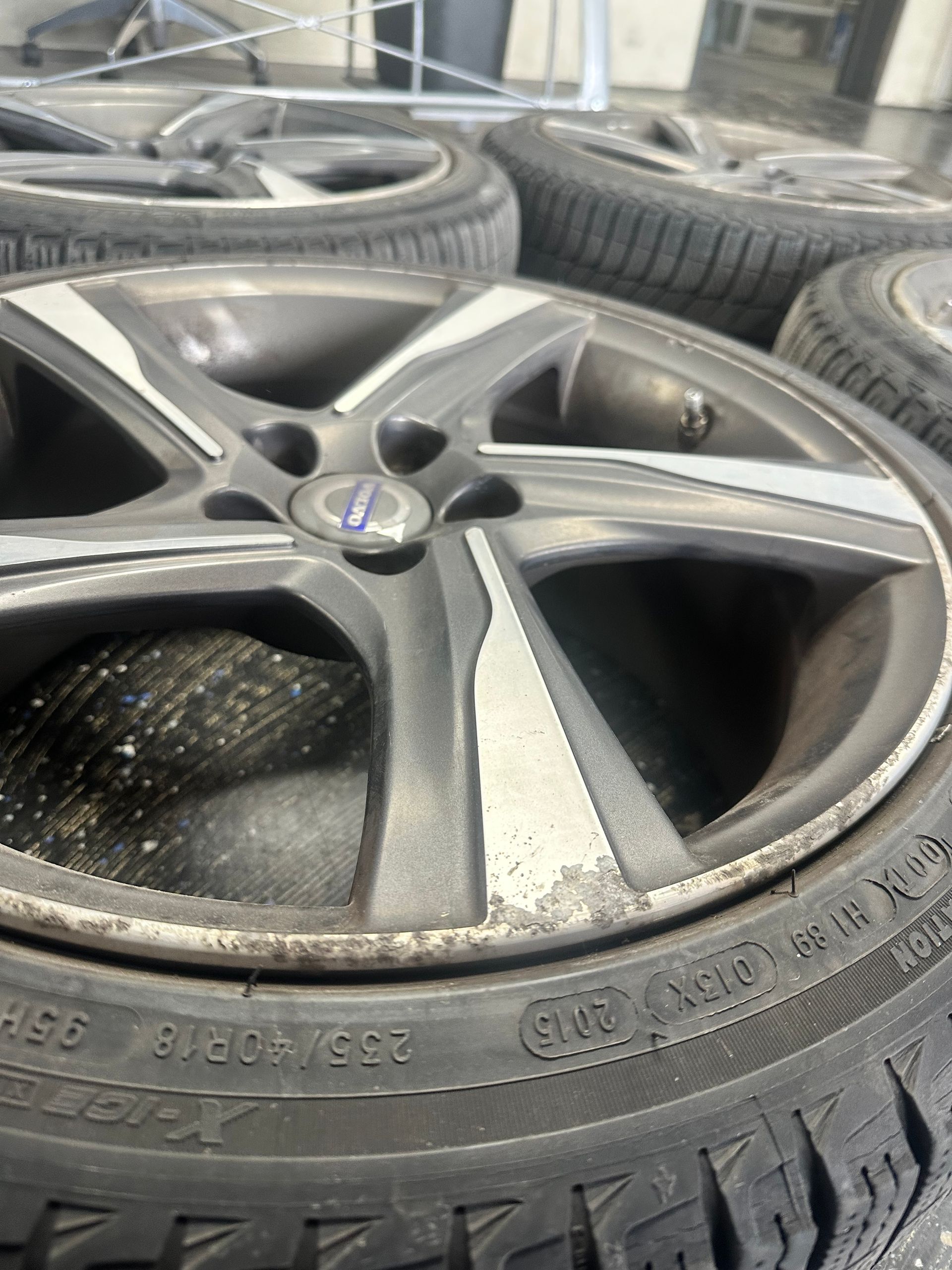 Close-up of a dirty Volvo wheel and tire. The wheel is silver and black, and the tire has snow tread.