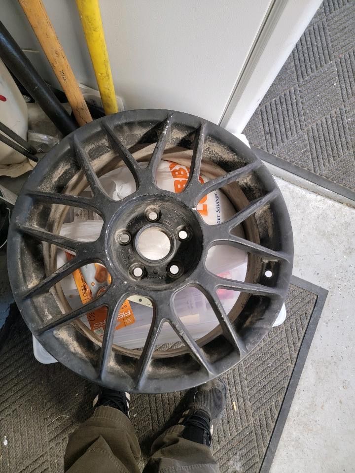 A person is standing next to a dirty wheel in a garage.